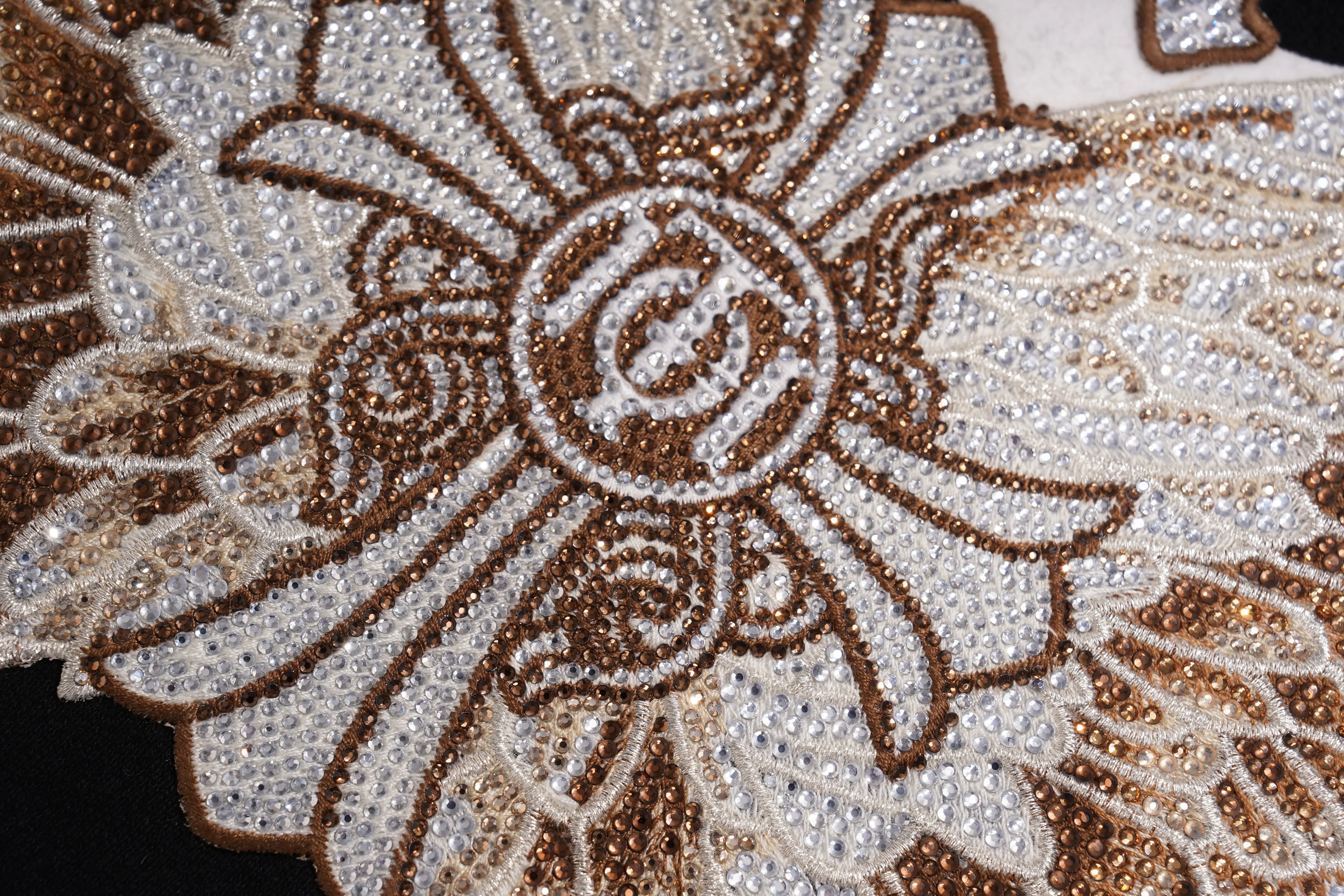 Close-up of a decorative design with floral patterns and a central emblem on a textured surface. TCH Rhinestone Wing M Embroidered Sweatshirt