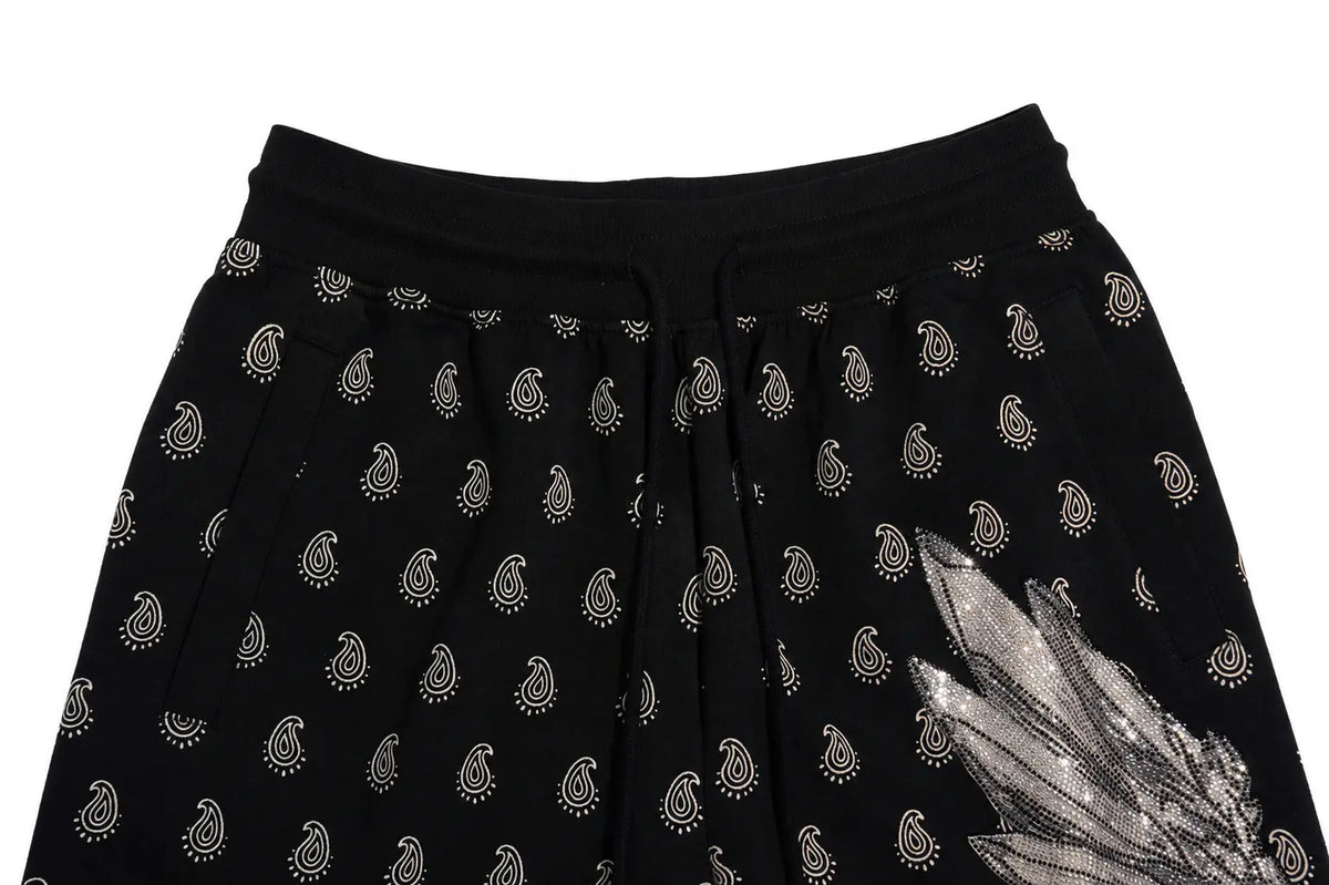 Black skirt with a repeating paisley pattern and a large metallic silver feather applique on the lower right side, shown against a plain white background. TCH Rhinestone Wing Paisley Wide-Leg Sweatpants
