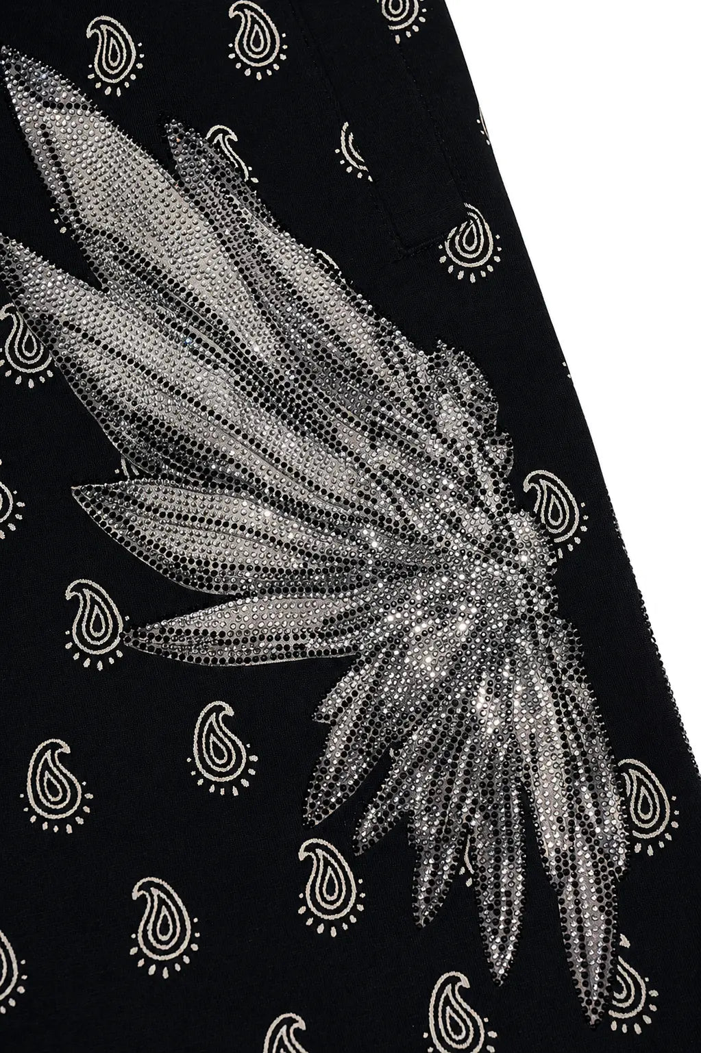 A close-up of a black fabric featuring a large silver beaded angel wing design and a repeating white paisley pattern. TCH Rhinestone Wing Paisley Wide-Leg Sweatpants