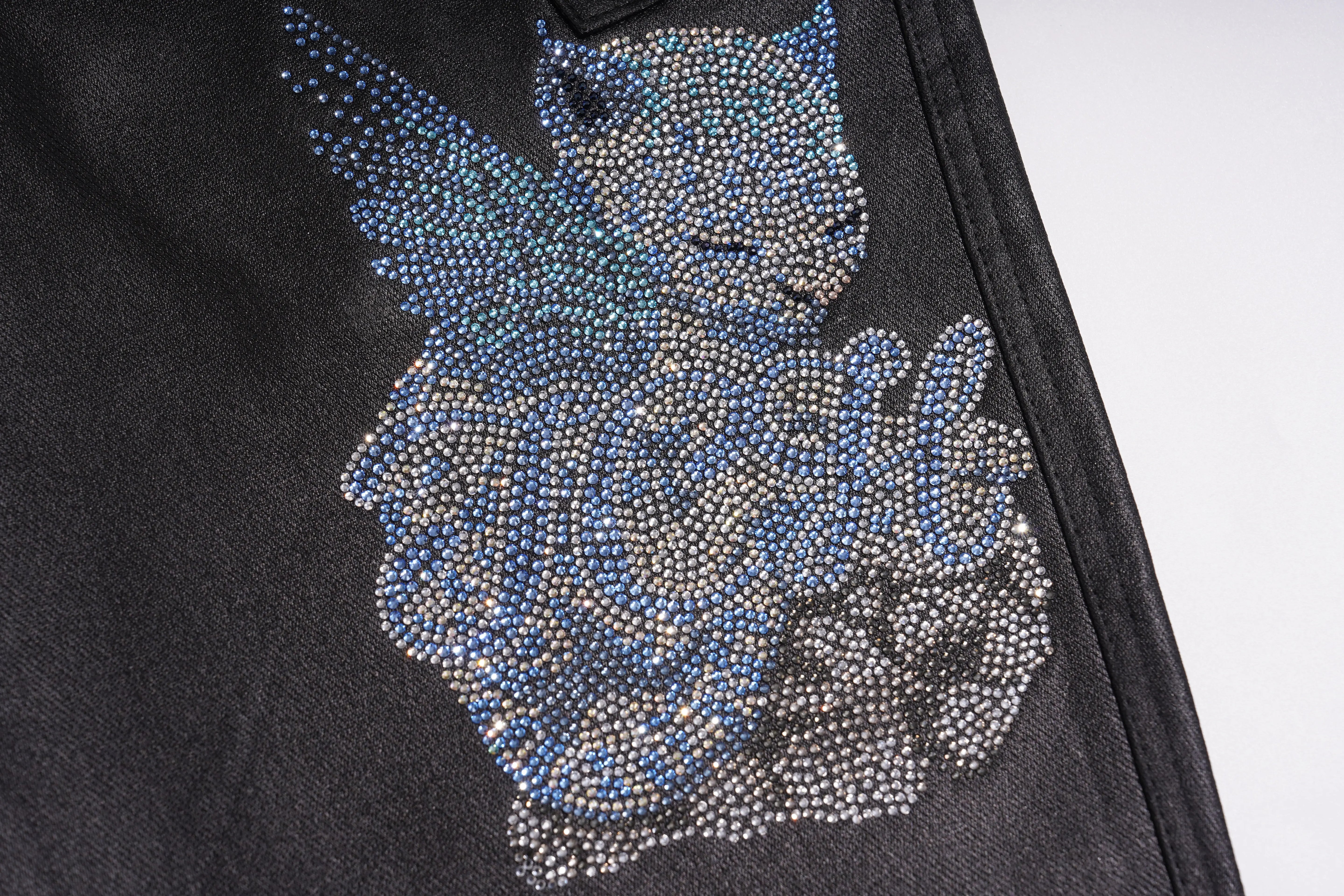 Close-up of a black denim garment featuring a large rhinestone-embellished angel graphic in shades of blue, silver, and gray. TCH Rhinestone Wing Teddy Faux Leather Jogger Pants