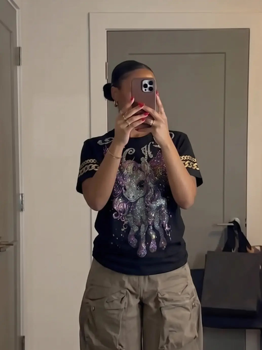 Person wearing a black t-shirt with a colorful graphic design and beige pants, standing in front of a mirror. TCH Rhinestone Winged Unicorn T-Shirt