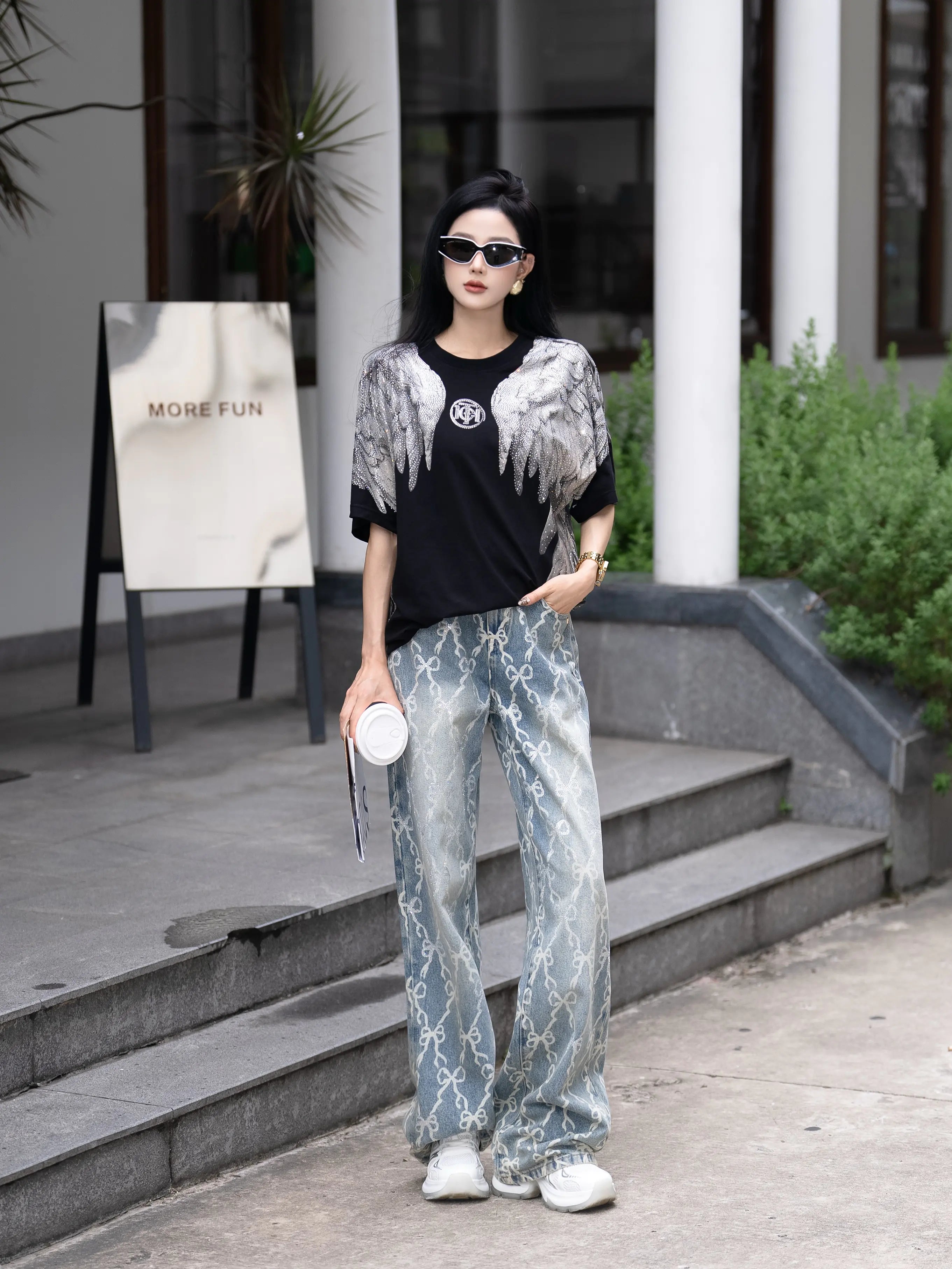 Woman in stylish outfit standing outdoors with a 'More Fun' sign in the background, TCH Rhinestone Wings Logo Black Graphic T-Shirt