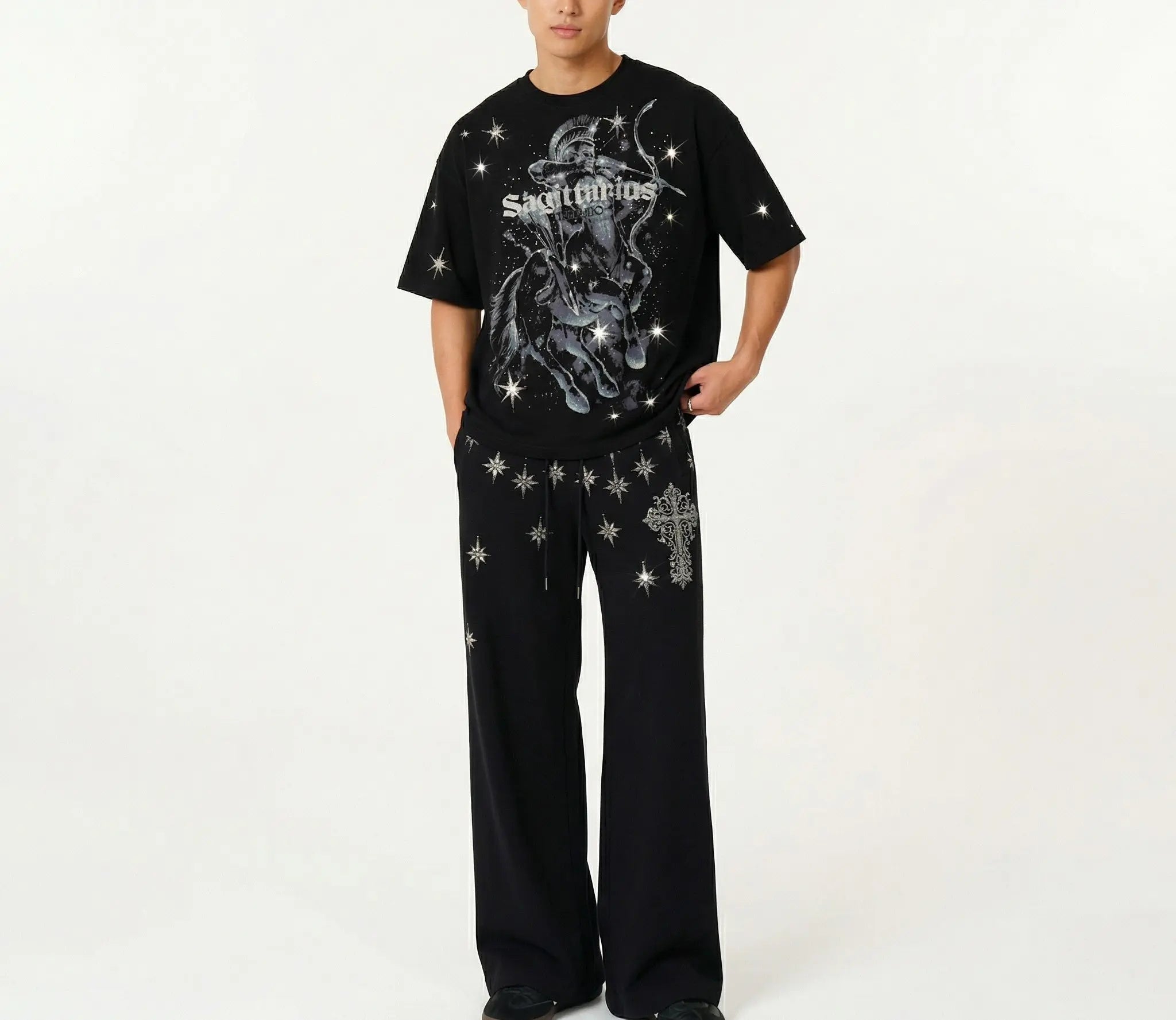 A model wearing a black t-shirt and matching wide-leg pants set from the band Skrillex, featuring silver graphic prints and star details, against a plain white studio background. TCH Sagittarius Celestial Graphic Oversized T-Shirt