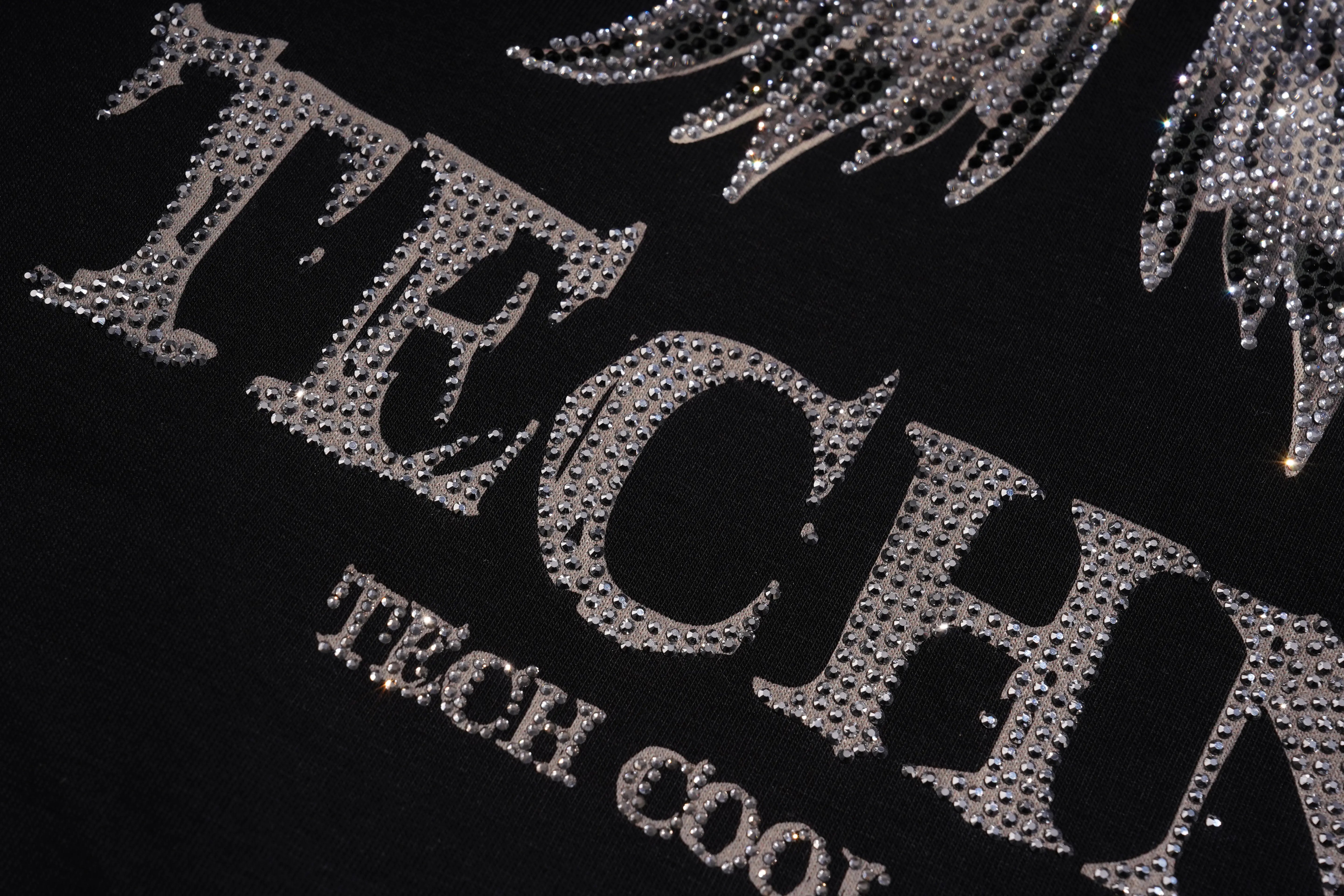A close-up of a mustard yellow woven fabric featuring a small crescent moon and star motif embellished with blue and clear rhinestones. TCH Silver Wing Techno Oversized Graphic T-Shirt