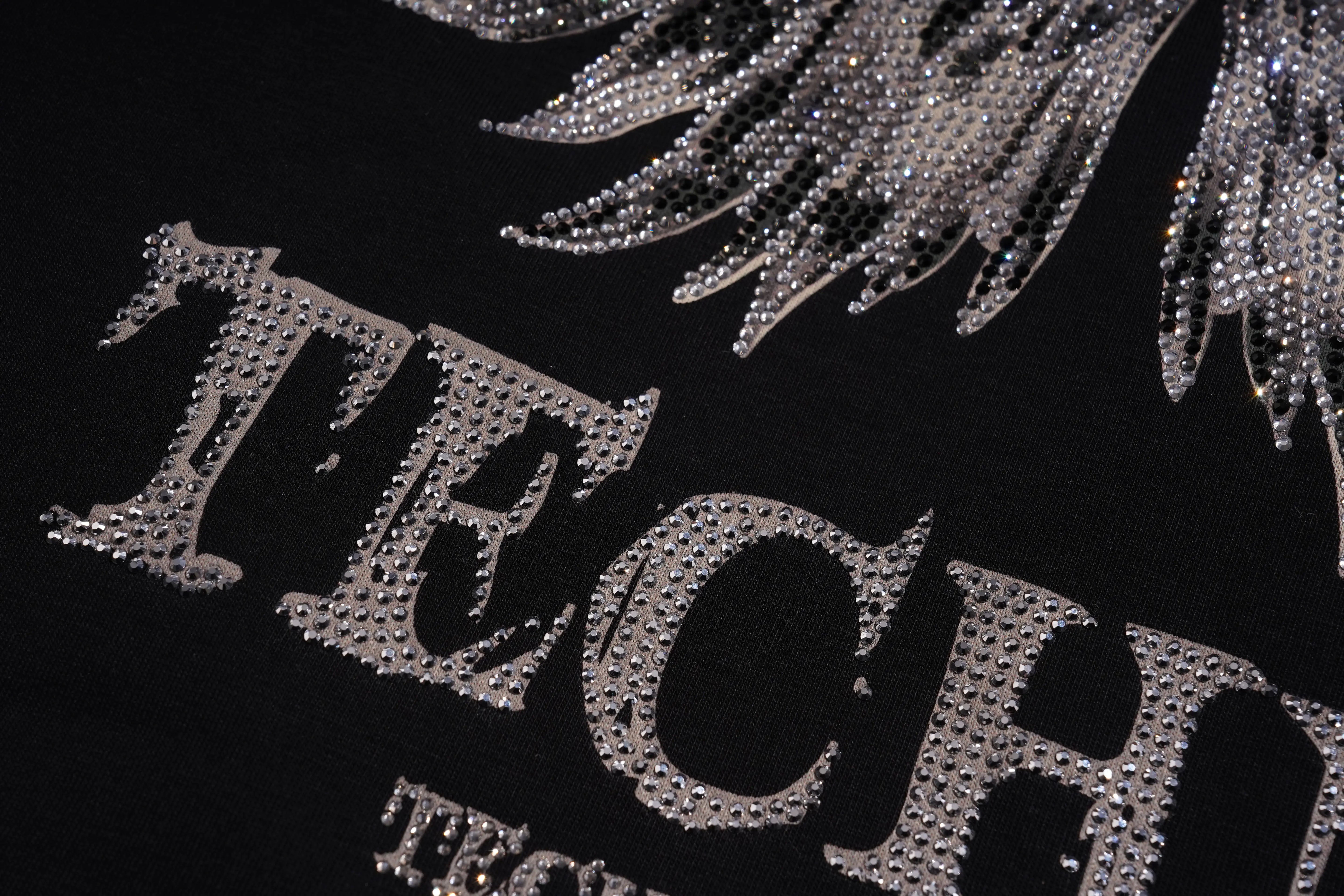 A close-up of a mustard yellow woven fabric featuring an embroidered crescent moon and star motif in iridescent rhinestones. TCH Silver Wing Techno Oversized Graphic T-Shirt