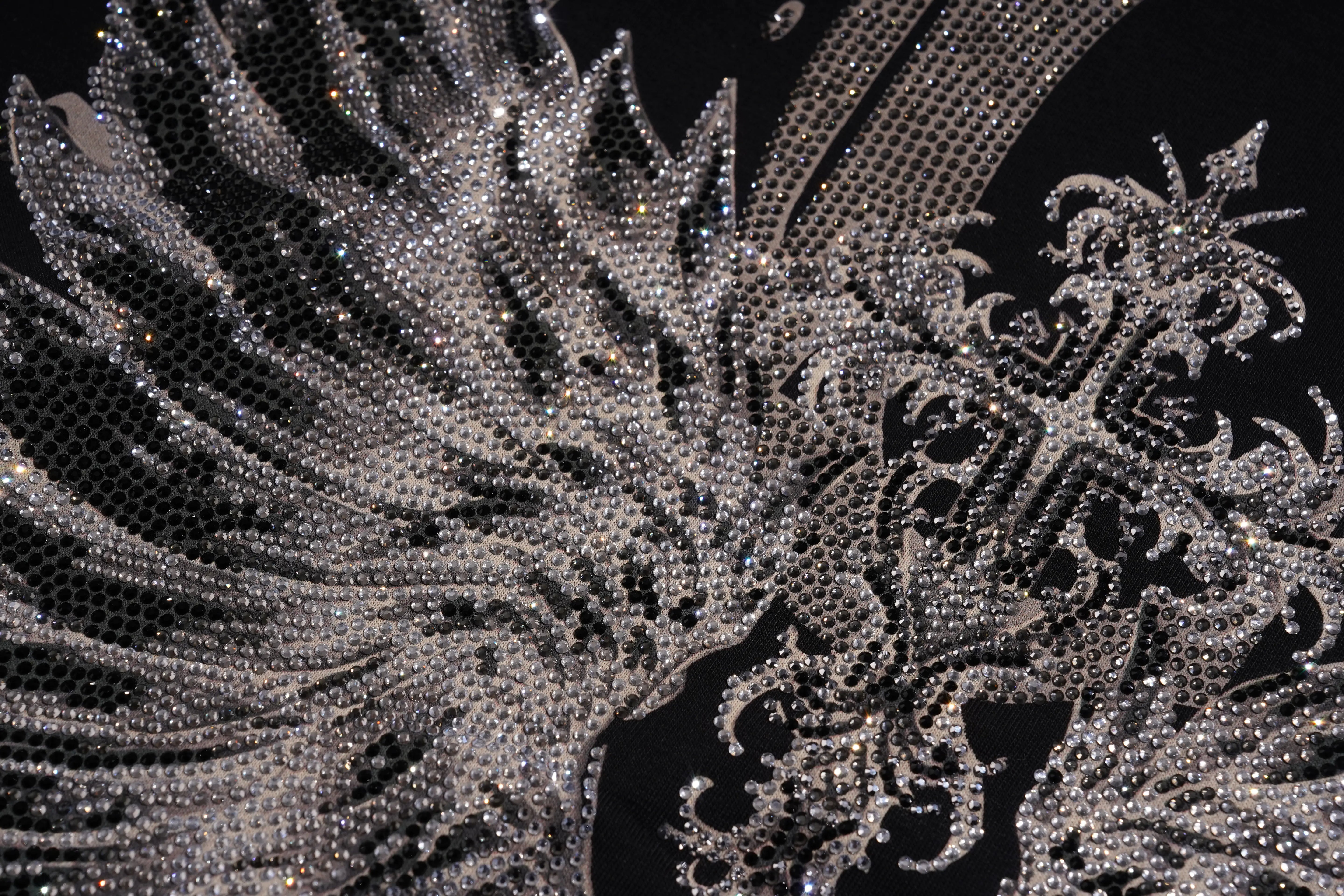 A close-up of an ornate silver rhinestone embellishment or decorative wing-like applique with intricate filigree and glittering crystal details on a black background. TCH Silver Wing Techno Oversized Graphic T-Shirt