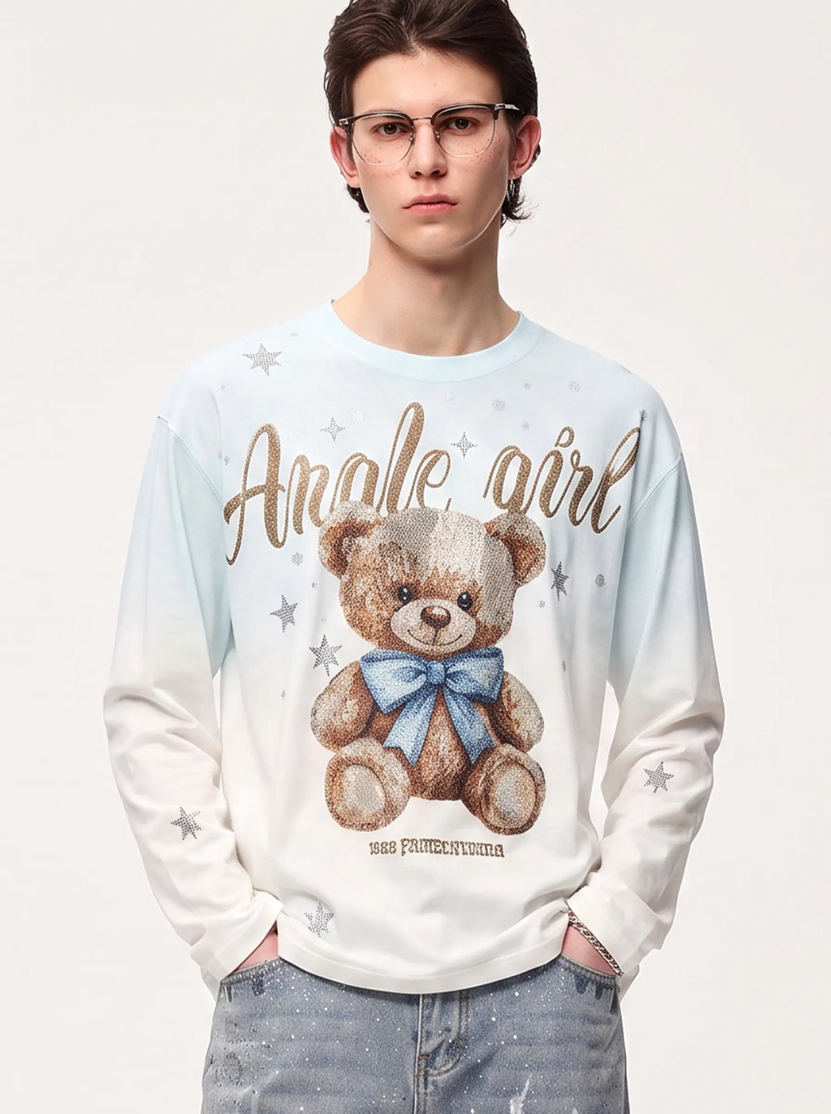 A model wearing a light blue denim jacket with various embroidered patches, including a teddy bear on the left chest and cherries on the sleeve, styled over a white t-shirt and dark pants. TCH Small Bear Angel Wings Rhinestone Graphic White Long Sleeve T-Shirt