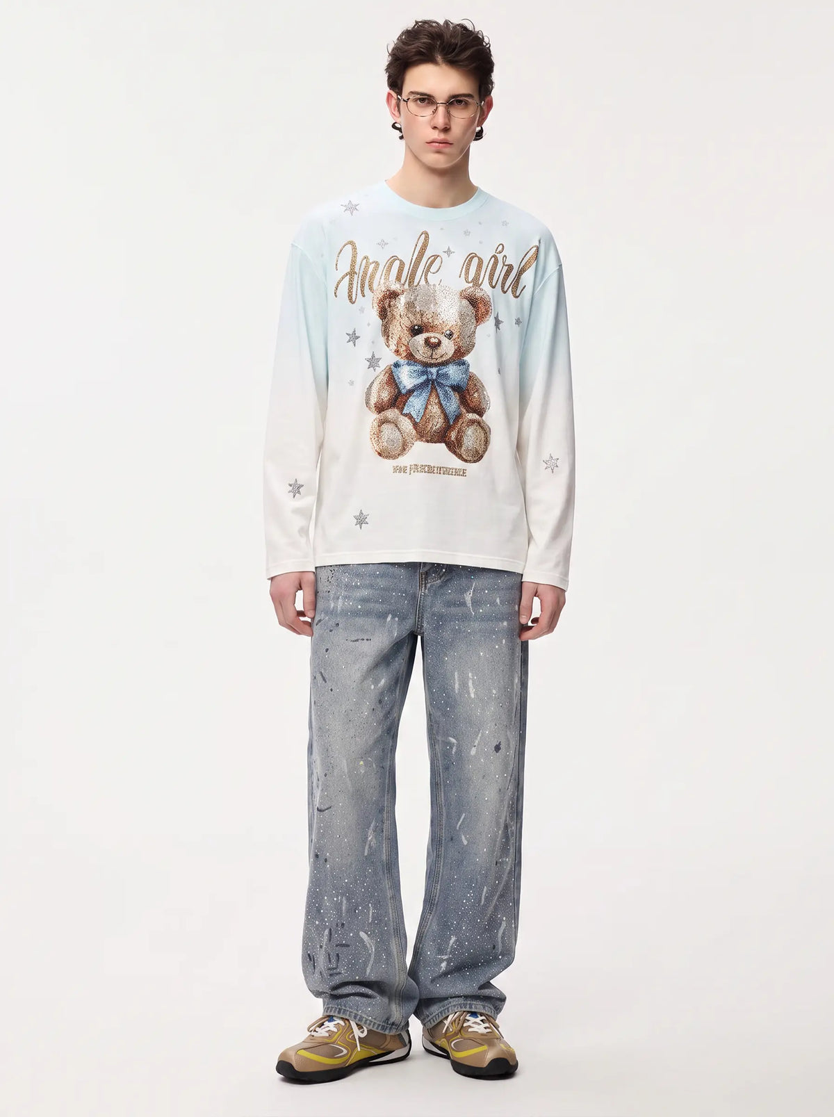 A model stands against a plain light background wearing a long-sleeve graphic sweatshirt with a teddy bear print and the words 'angel girl', paired with light blue jeans and gold sneakers. TCH Small Bear Angel Wings Rhinestone Graphic White Long Sleeve T-Shirt