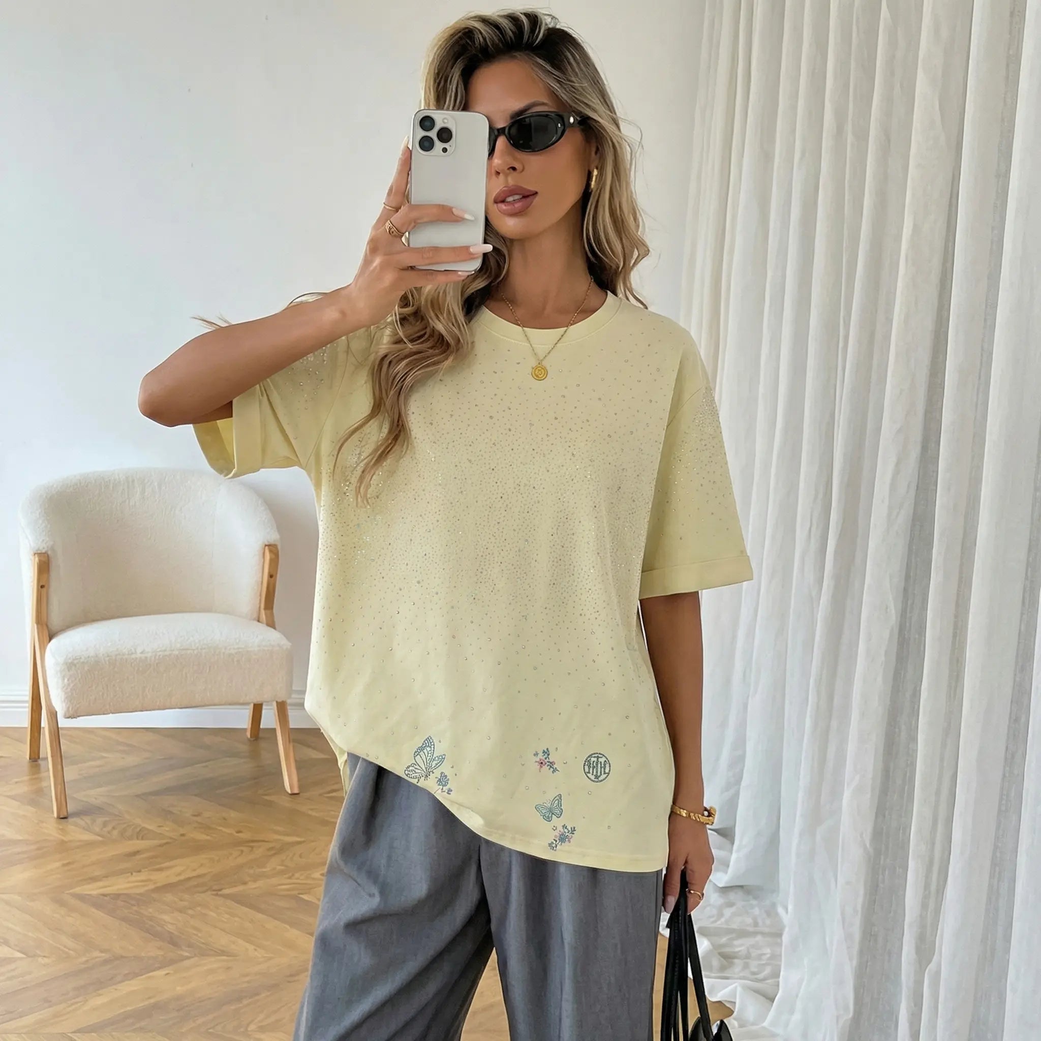 Woman taking a mirror selfie wearing a light yellow oversized t-shirt with floral embroidery and gray pants in a room. TCH Starry Gradient Rhinestone Butterfly T-Shirt