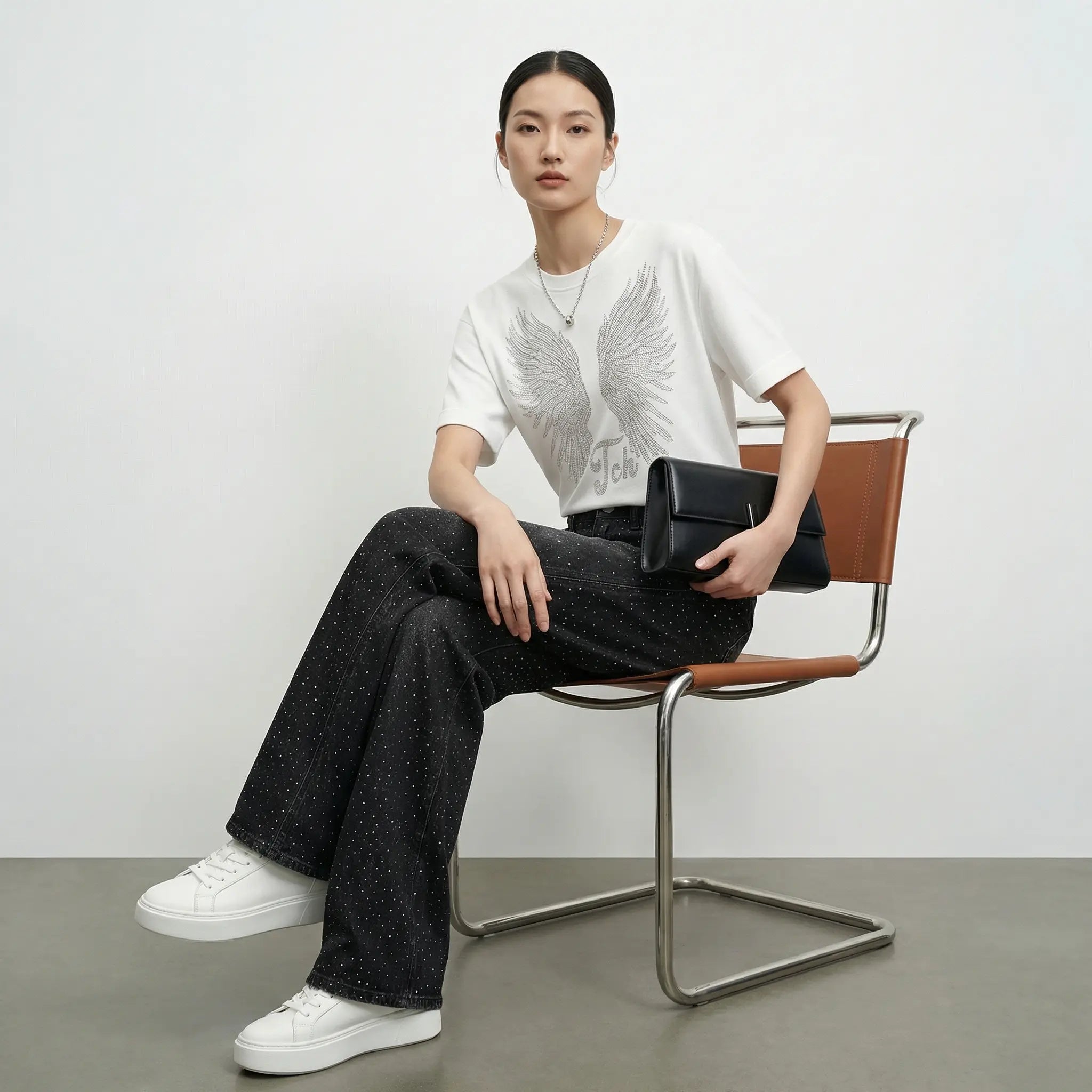 Person sitting on a chair holding a black clutch against a plain background, TCH Starry Rhinestone Logo Black Denim Jeans