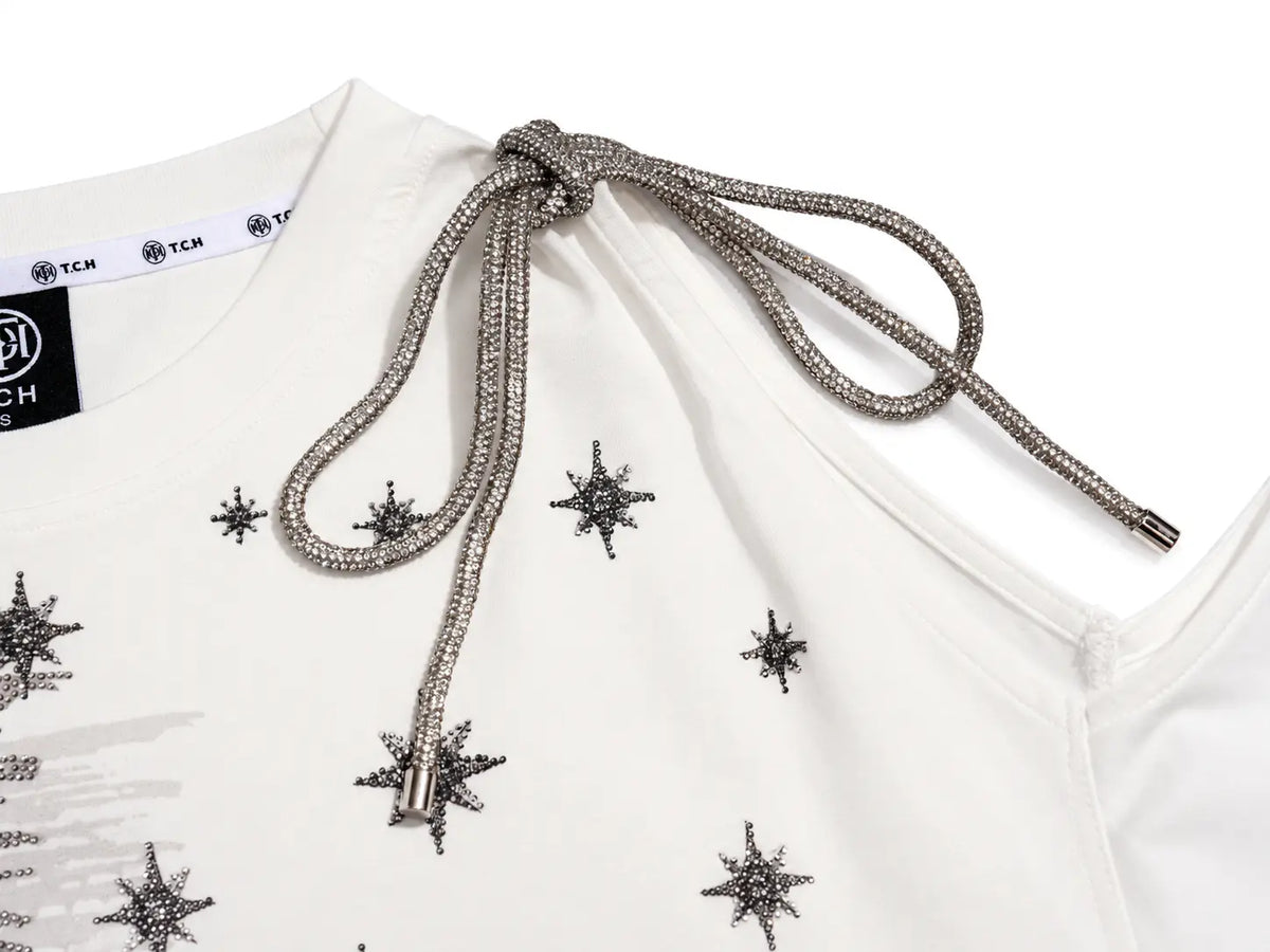 Close-up of a white top with silver rhinestone star embellishments and a matching silver rhinestone drawstring tie at the neckline. TCH Starry Western Graphic White Long Sleeve Top