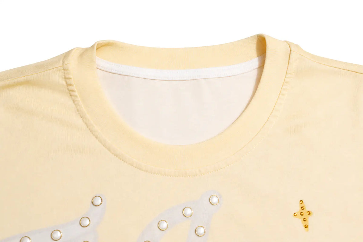 Close-up of a pale yellow t-shirt showing the inner collar, white ribbed neckband, and decorative gold and white studs on the front. TCH Sweet Bunny Rhinestone Graphic Long Sleeve Top