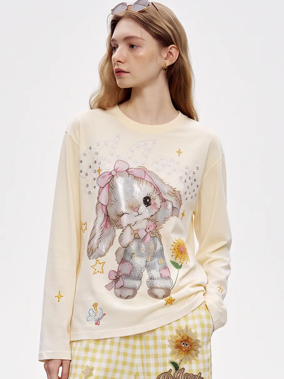 A model wearing a light blue denim jacket with various embroidered patches, including a teddy bear on the left chest and cherries on the sleeve, styled over a white t-shirt and dark pants. TCH Sweet Bunny Rhinestone Graphic Long Sleeve Top