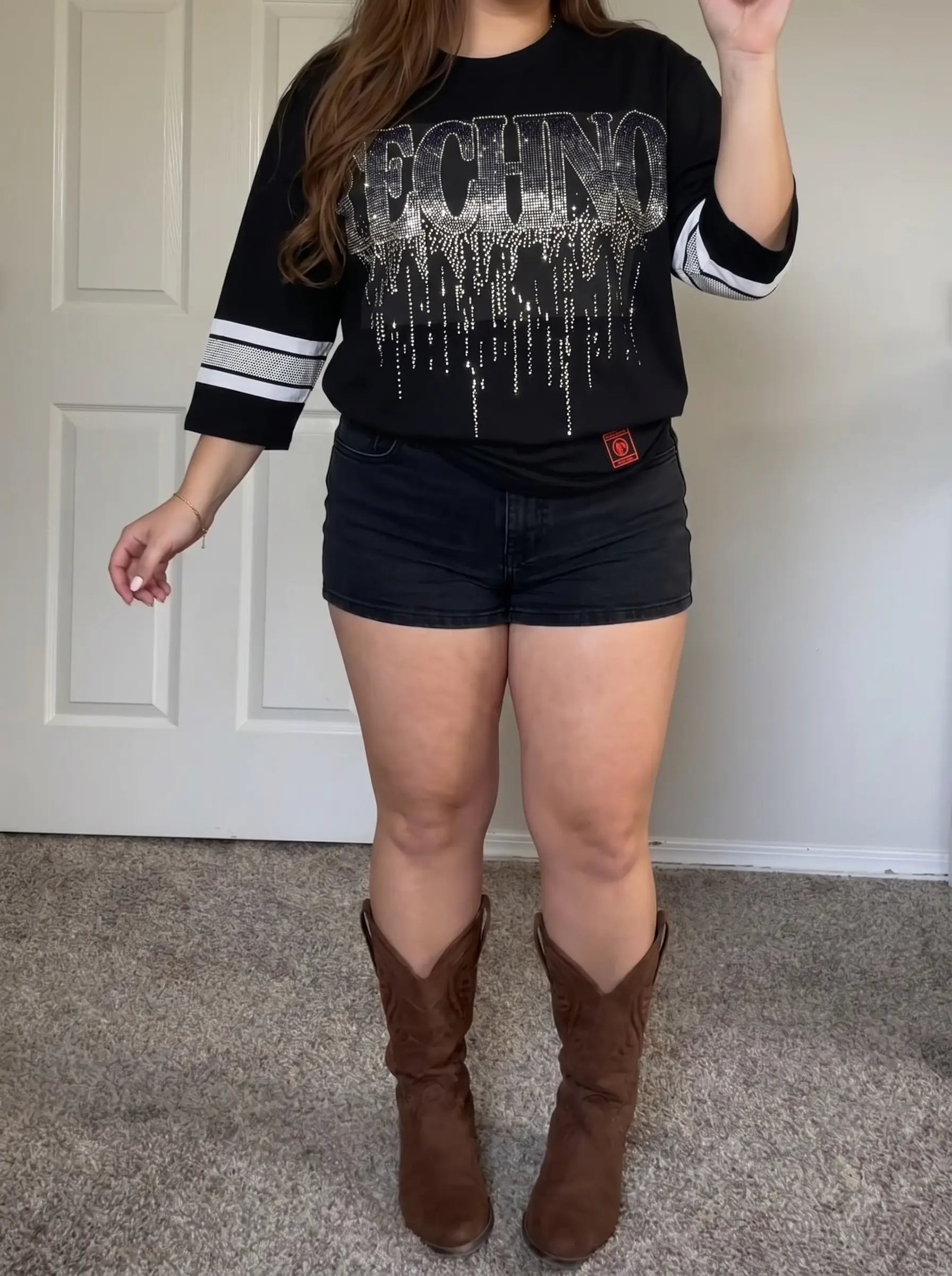 Person wearing a black sweatshirt with white text, black shorts, and brown cowboy boots indoors. TCH TECHNO Waterfall Rhinestone T-Shirt