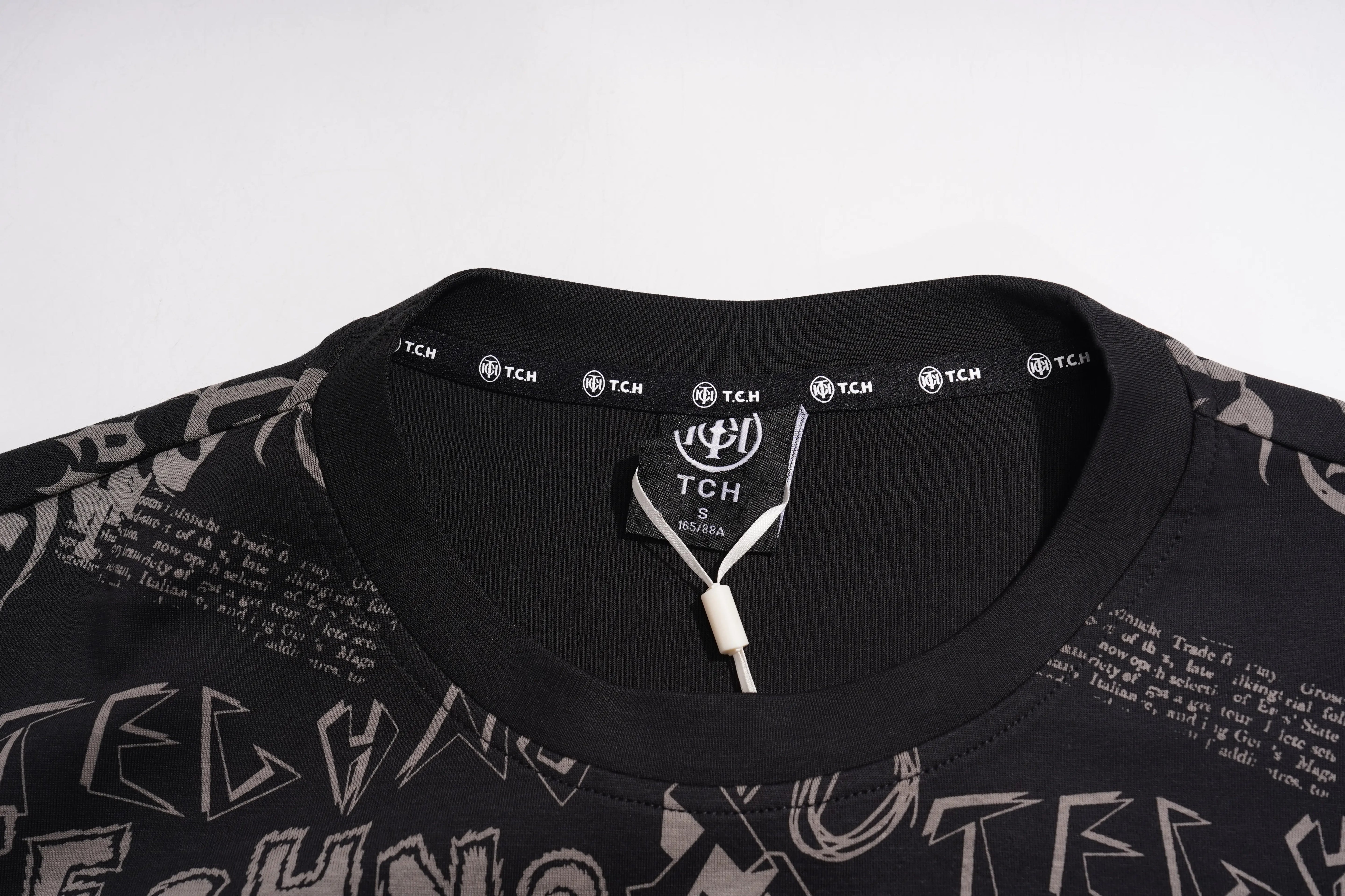 Close-up of a black TCGI T-shirt collar with a white drawstring and a black neck label featuring the TCGI logo and repeated TCGI text, set against a plain light background. TCH Techno Graffiti Rhinestone Skull Oversized T-Shirt