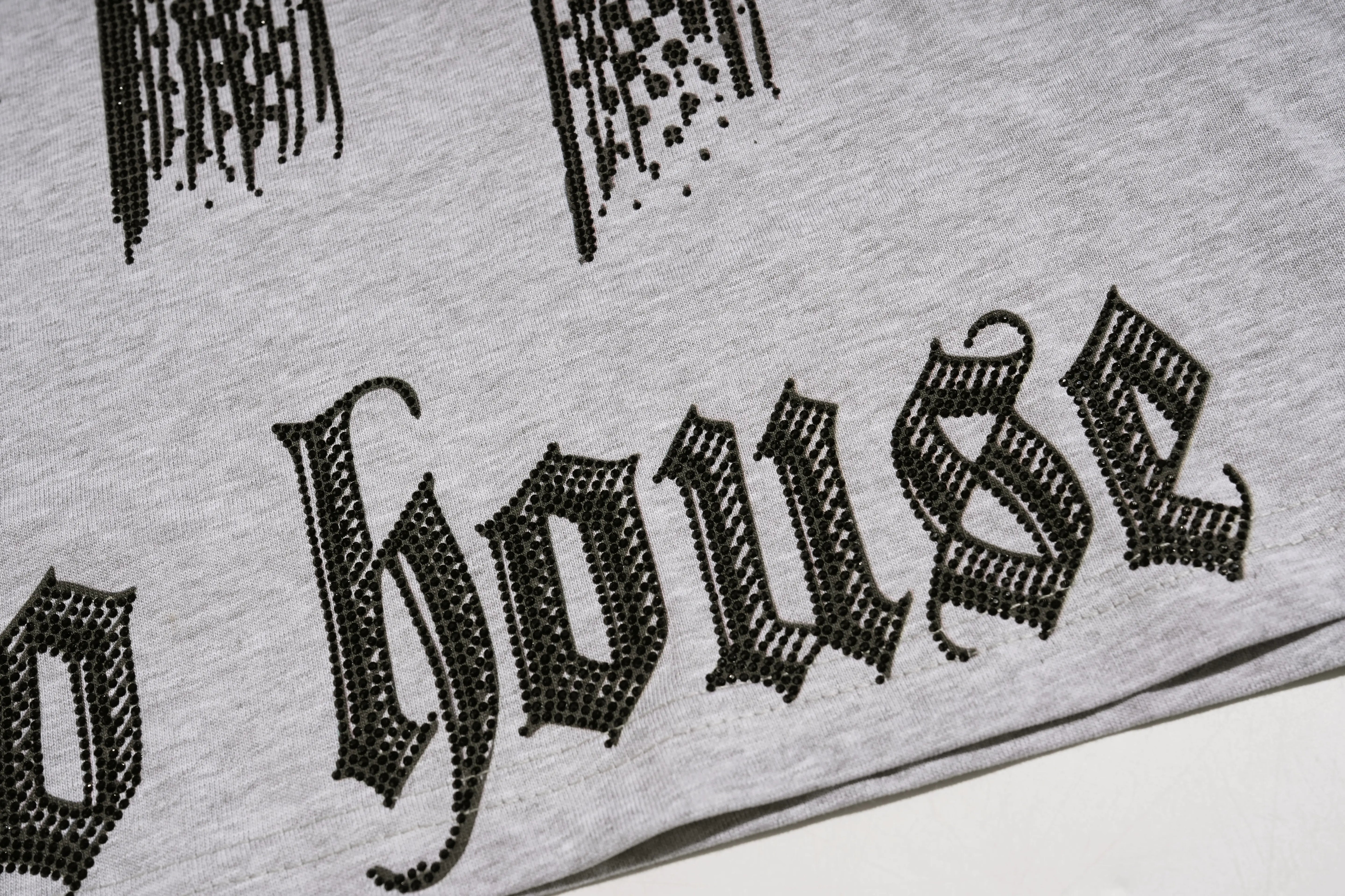 Close-up of a light gray heathered fabric with a black gothic-style printed word reading "house" and partial graphic elements above it. TCH Techno House Abstract Graphic Oversized T-Shirt