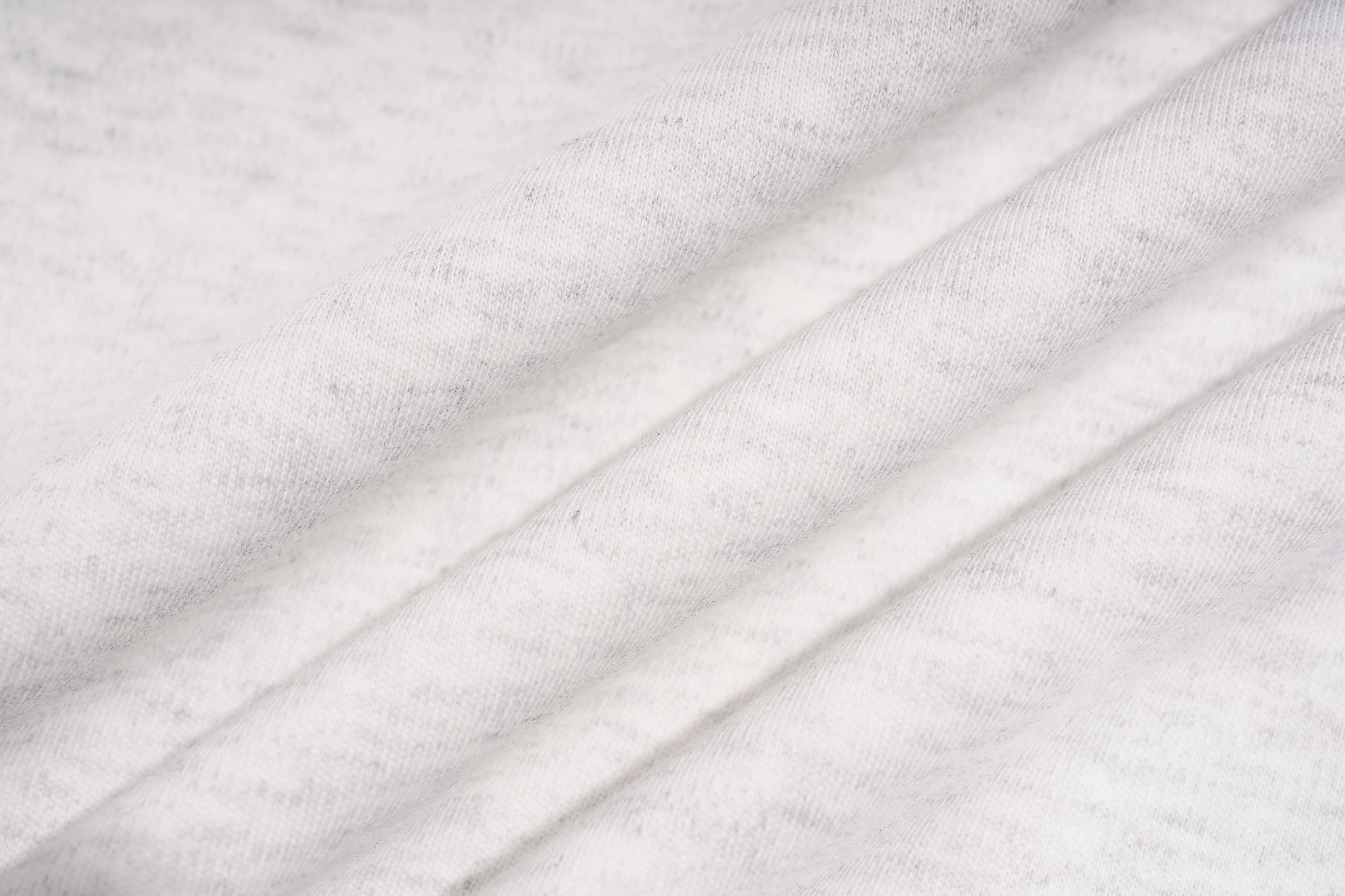 A close-up of white heathered fabric with soft diagonal folds showing a fine knit texture. TCH Techno House Wing Graphic Oversized T-Shirt