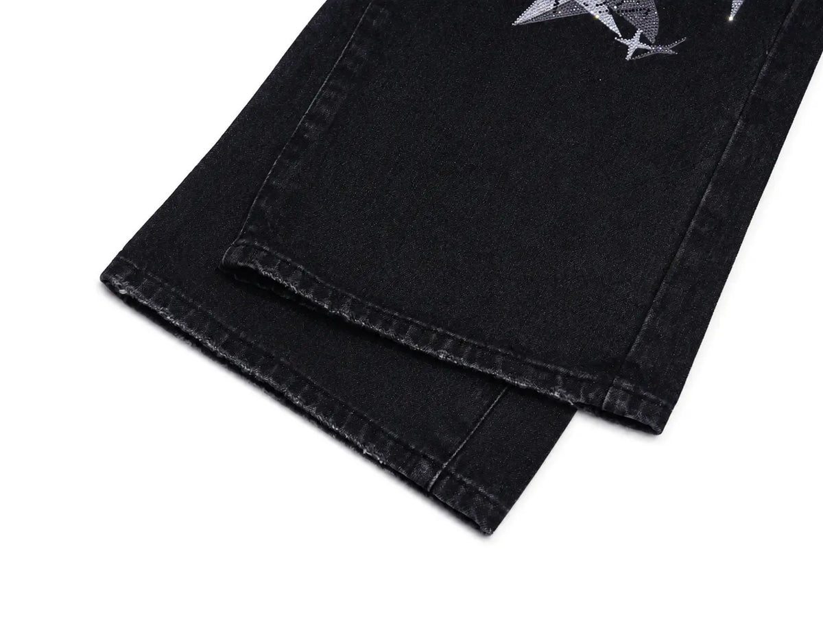 Close-up of folded black denim jeans on a white background, showing the hem and a small gray graphic print near the upper leg. TCH Techno Magic Star Graphic Wide-Leg Jeans