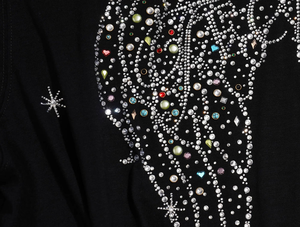 Close-up of a black garment featuring an elaborate rhinestone and bead embellishment in a wing-like pattern, with small multicolored crystals and silver starburst details. TCH Techno Rhinestone Angel Wings Lace Trim Off-Shoulder Top