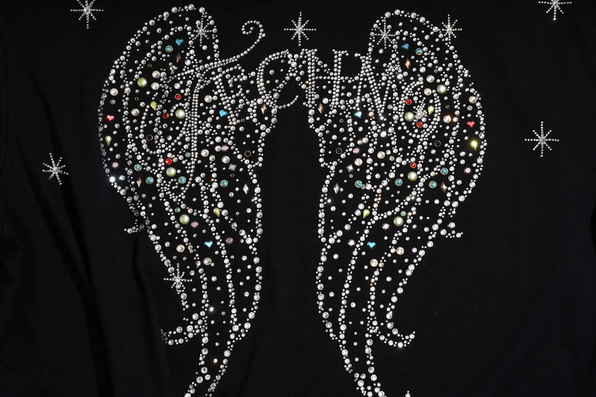 A close-up of a black garment featuring a large rhinestone angel wing design with the word 'KICHING' spelled across the wings in silver and multicolor rhinestones, accented with small star-shaped rhinestone motifs. TCH Techno Rhinestone Angel Wings Lace Trim Off-Shoulder Top