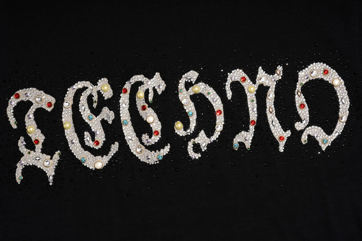 A close-up of a black garment featuring the word 'SECOND' spelled out in ornate gothic-style letters embellished with silver rhinestones and small multicolored gem accents. TCH Techno Rhinestone Gothic Graphic Black T-Shirt