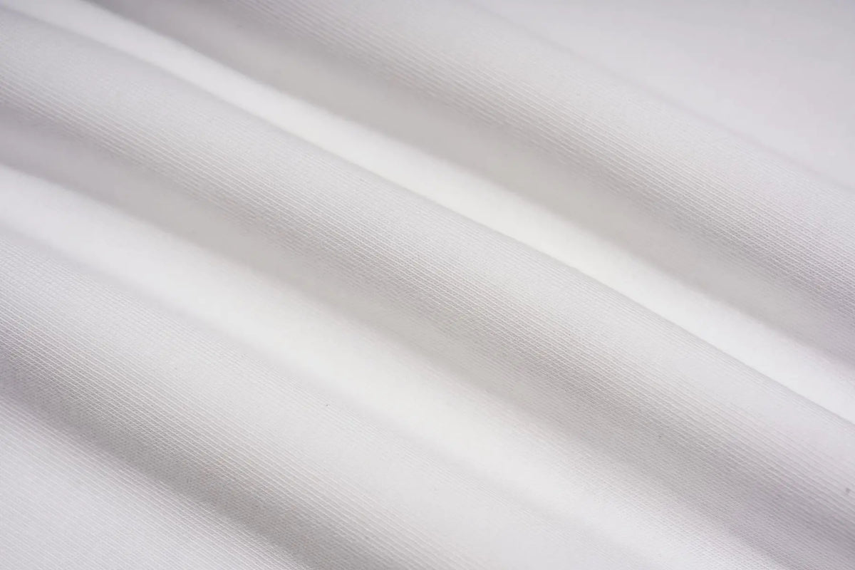 A close-up of draped white fabric with soft folds and a fine woven texture. TCH Techno Teddy Graphic Raglan Long Sleeve Shirt