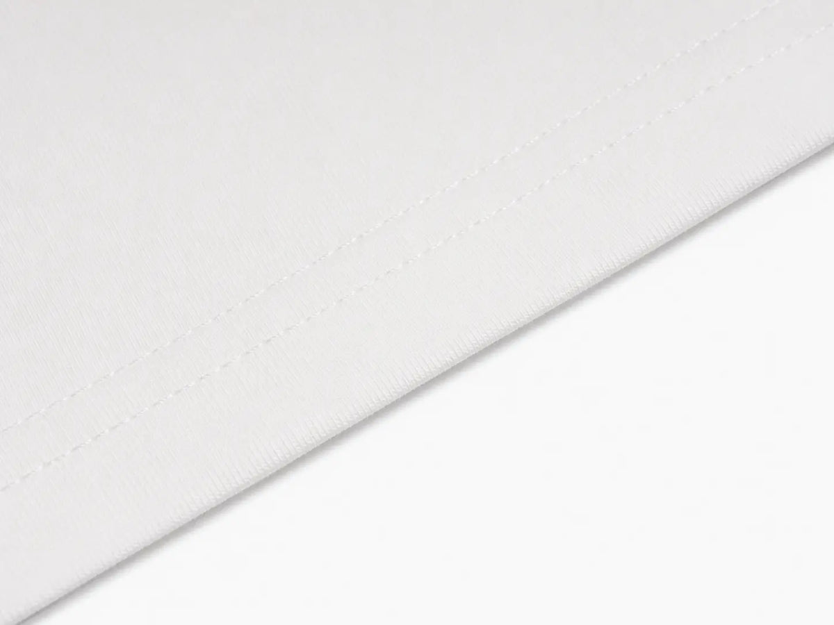 A close-up of a white fabric surface with a diagonal fold showing fine texture and subtle stitching. TCH Techno Teddy Graphic Raglan Long Sleeve Shirt