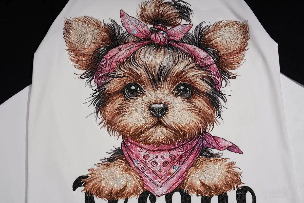 A close-up of a white garment featuring a detailed graphic illustration of a Yorkshire Terrier dog wearing a pink bandana, with black text partially visible below. TCH Techno Teddy Graphic Raglan Long Sleeve Shirt