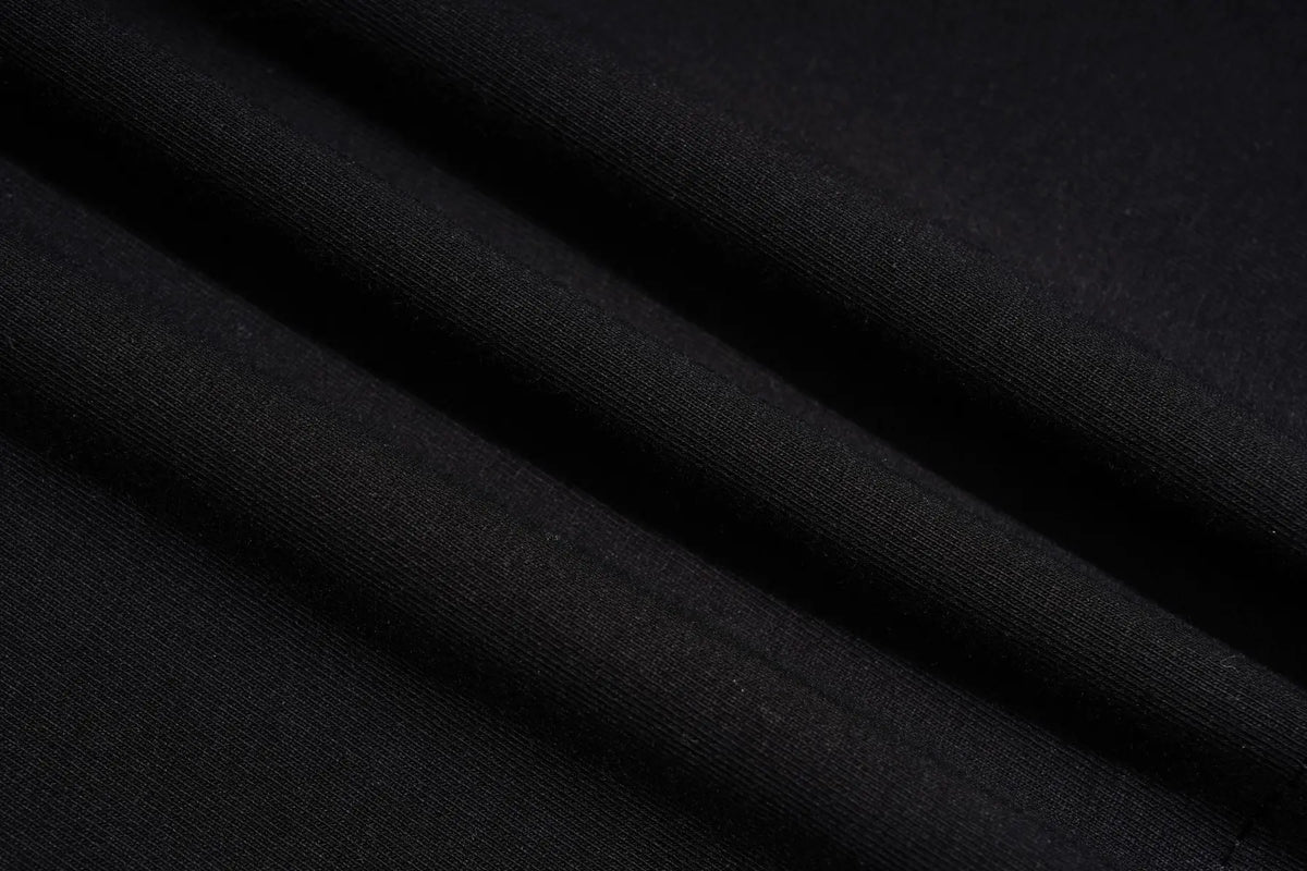 A close-up of draped black fabric with soft folds showing a fine knit texture. TCH Teddy Bear Charm Tie Graphic Black Long Sleeve T-Shirt