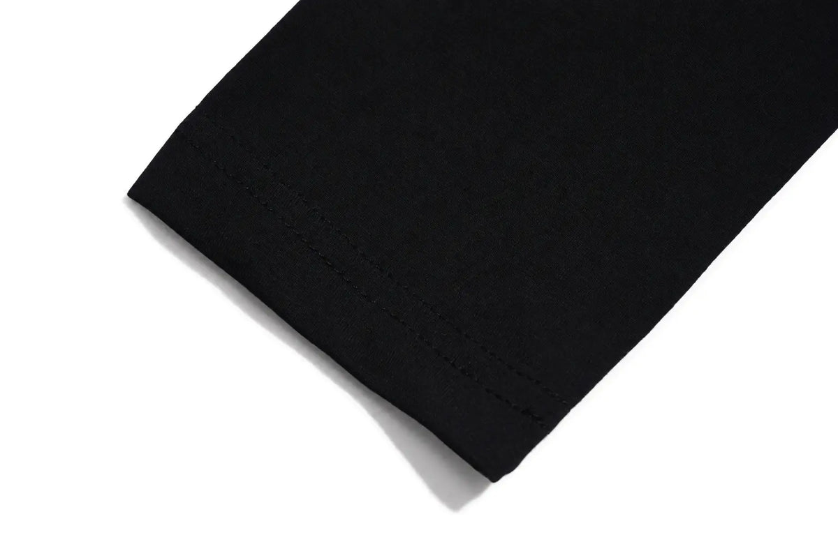Close-up of a black fabric cuff with neat hem stitching, shown on a plain white background. TCH Teddy Bear Charm Tie Graphic Black Long Sleeve T-Shirt