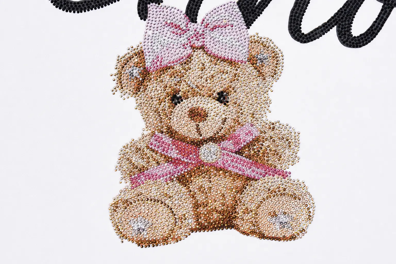 A teddy bear embellished with rhinestones, featuring a pink bow on its head and a pink ribbon around its neck, set against a white background with a partial black script at the top. TCH Teddy Bear Rhinestone All-Over Graphic T-Shirt