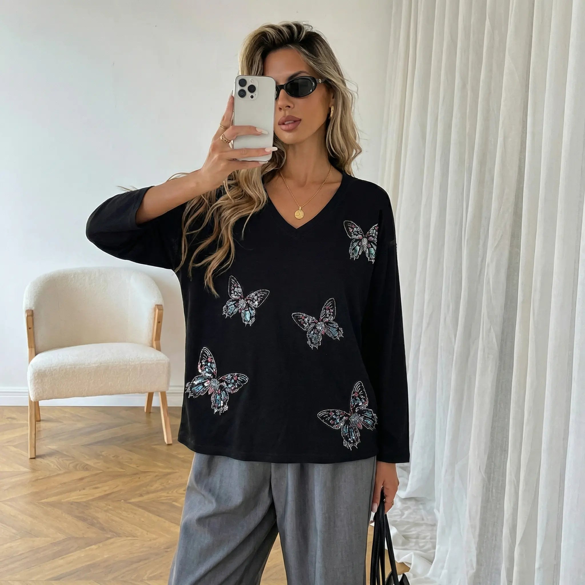 Woman taking a mirror selfie wearing a black sweater with butterfly designs in a room. TCH V-Neck Rhinestone Butterfly Long Sleeve Top