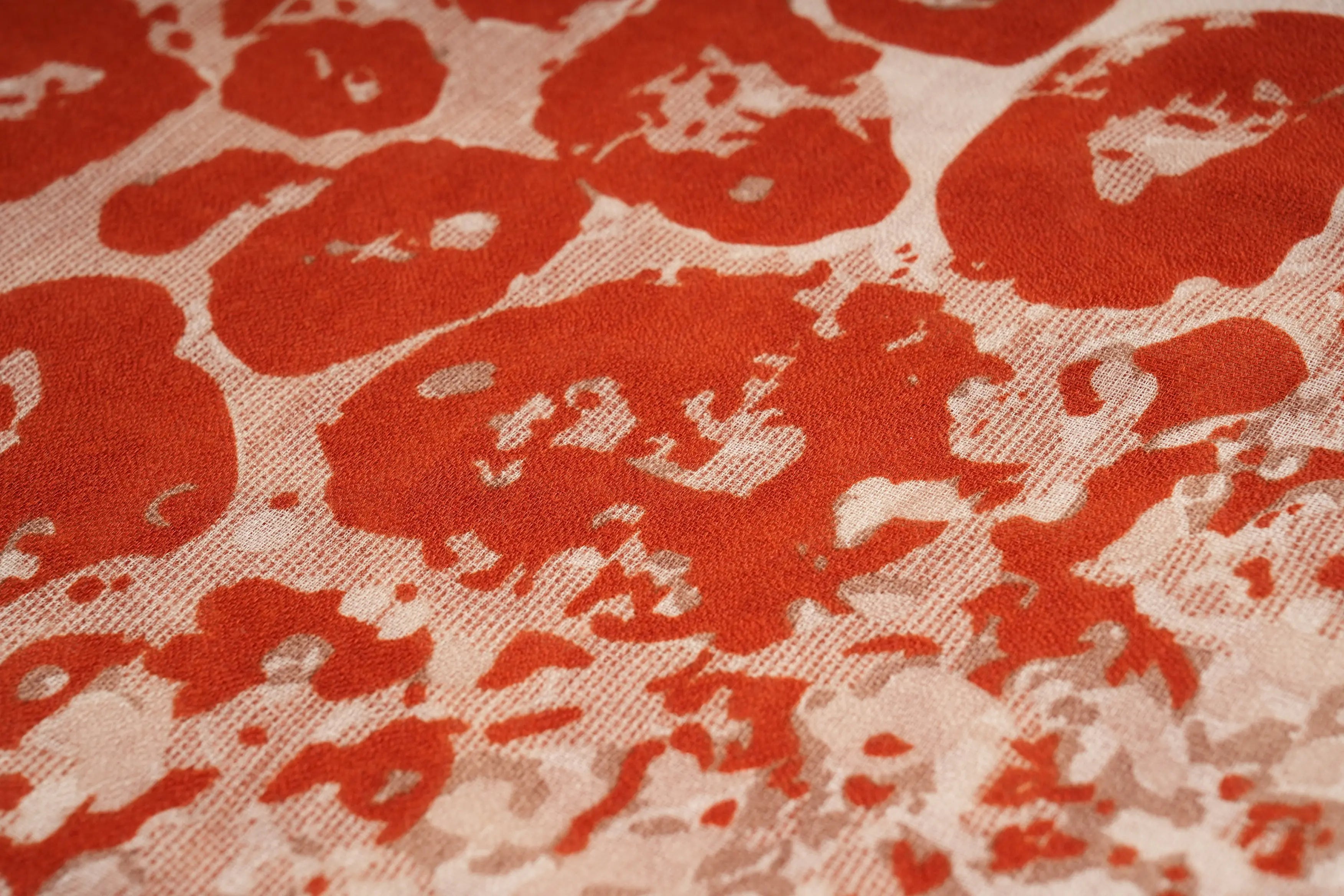 A close-up of a textured fabric featuring a bold, abstract pattern of rust-red splotches on a warm beige background. TCH Vintage Leopard Print Lightweight Fashion Scarf
