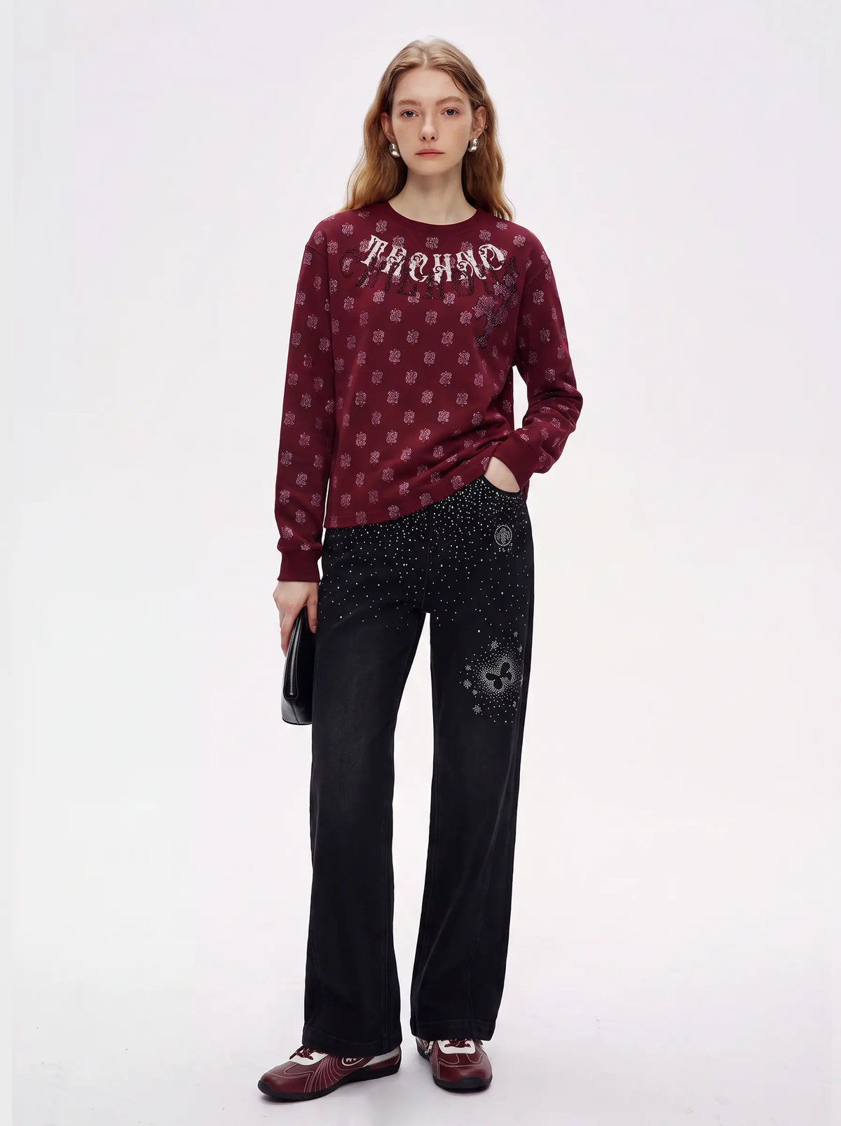 A model stands against a plain white studio background wearing a burgundy long-sleeve top with a repeating monogram pattern and the word 'ARCHMO' across the chest, paired with black wide-leg pants featuring a black-on-black leopard print patch on the lower right leg. TCH Vintage Paisley Graphic Burgundy Crewneck Sweatshirt