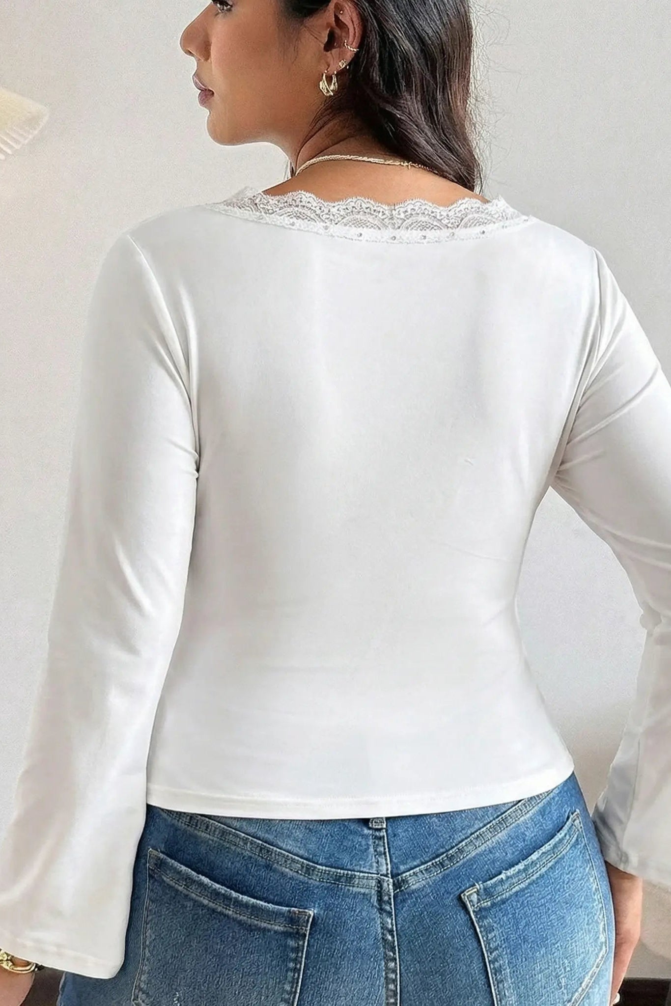 Woman wearing a white long-sleeve top with lace trim and blue jeans indoors. TCH White Lace Trim V-Neck Rhinestone Wing Long Sleeve Top