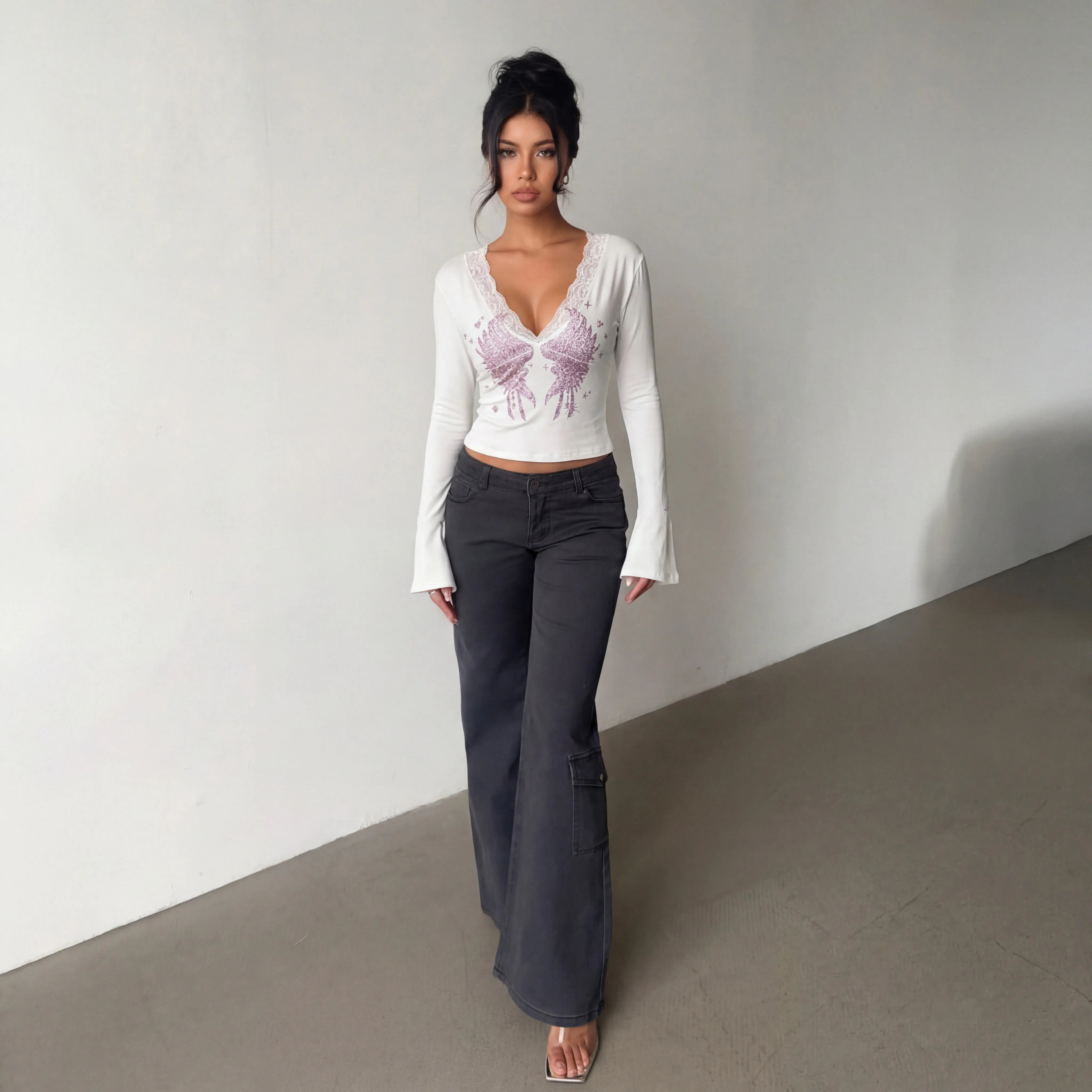 Woman wearing a white long-sleeve top with a purple design and dark pants against a plain background, TCH White Lace Trim V-Neck Rhinestone Wing Long Sleeve Top