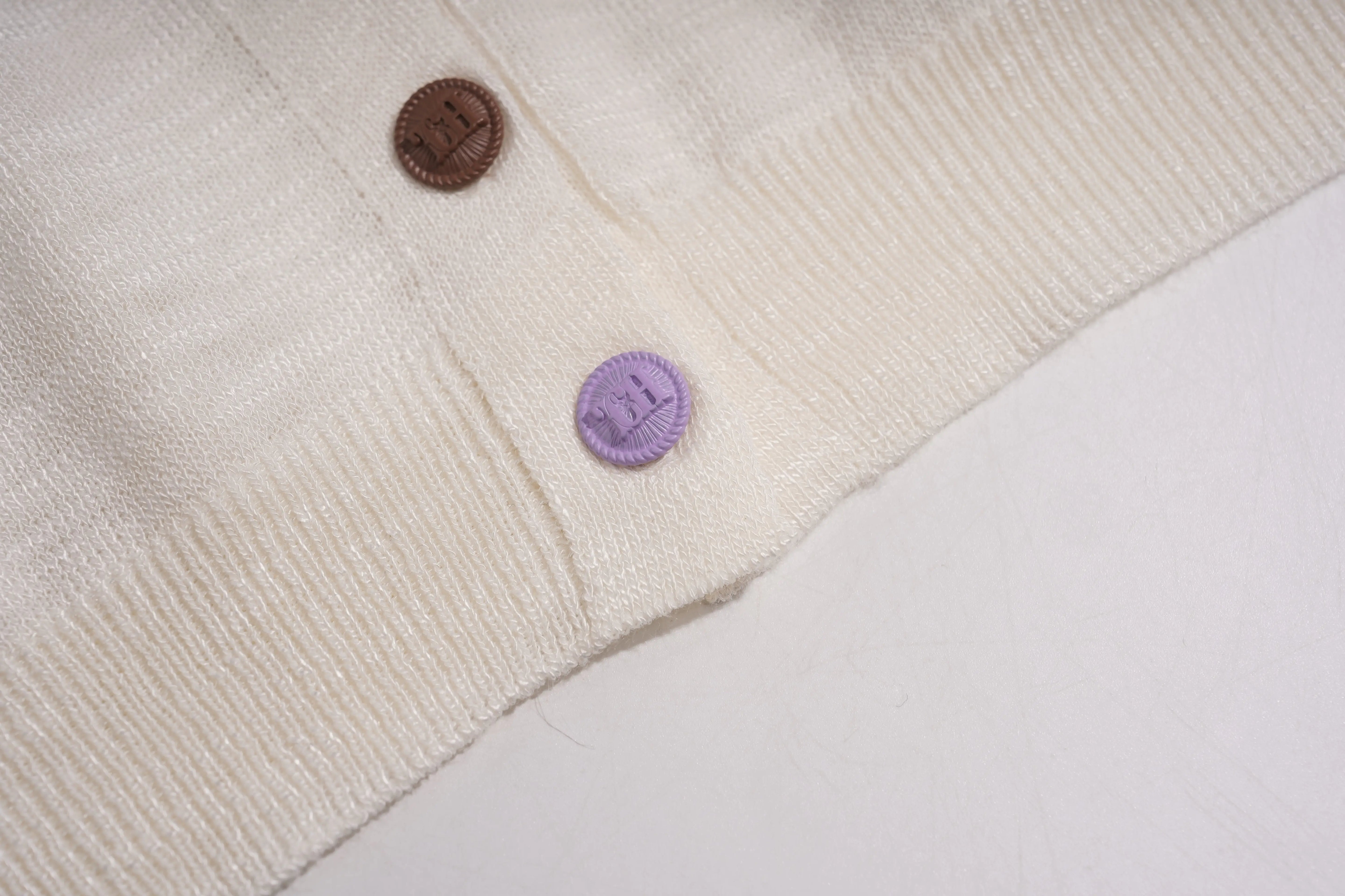 Close-up of a cream-colored cardigan with a brown button and a purple tag on a white background, TCH White Rhinestone Bow Knit Cardigan
