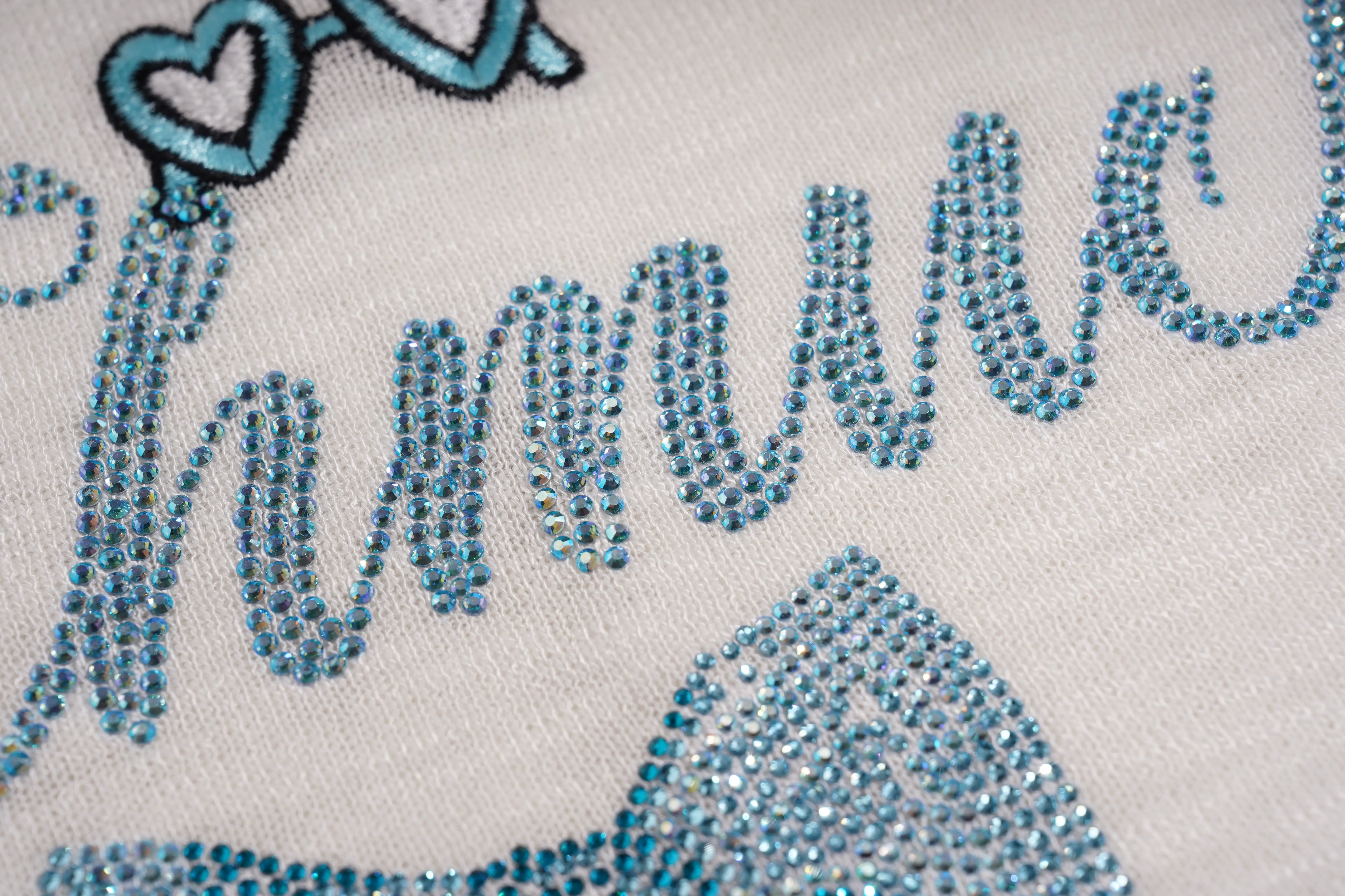 Close-up of a decorative item with blue rhinestones spelling out 'Harlow' on a light background. TCH White Rhinestone Bow Knit Cardigan