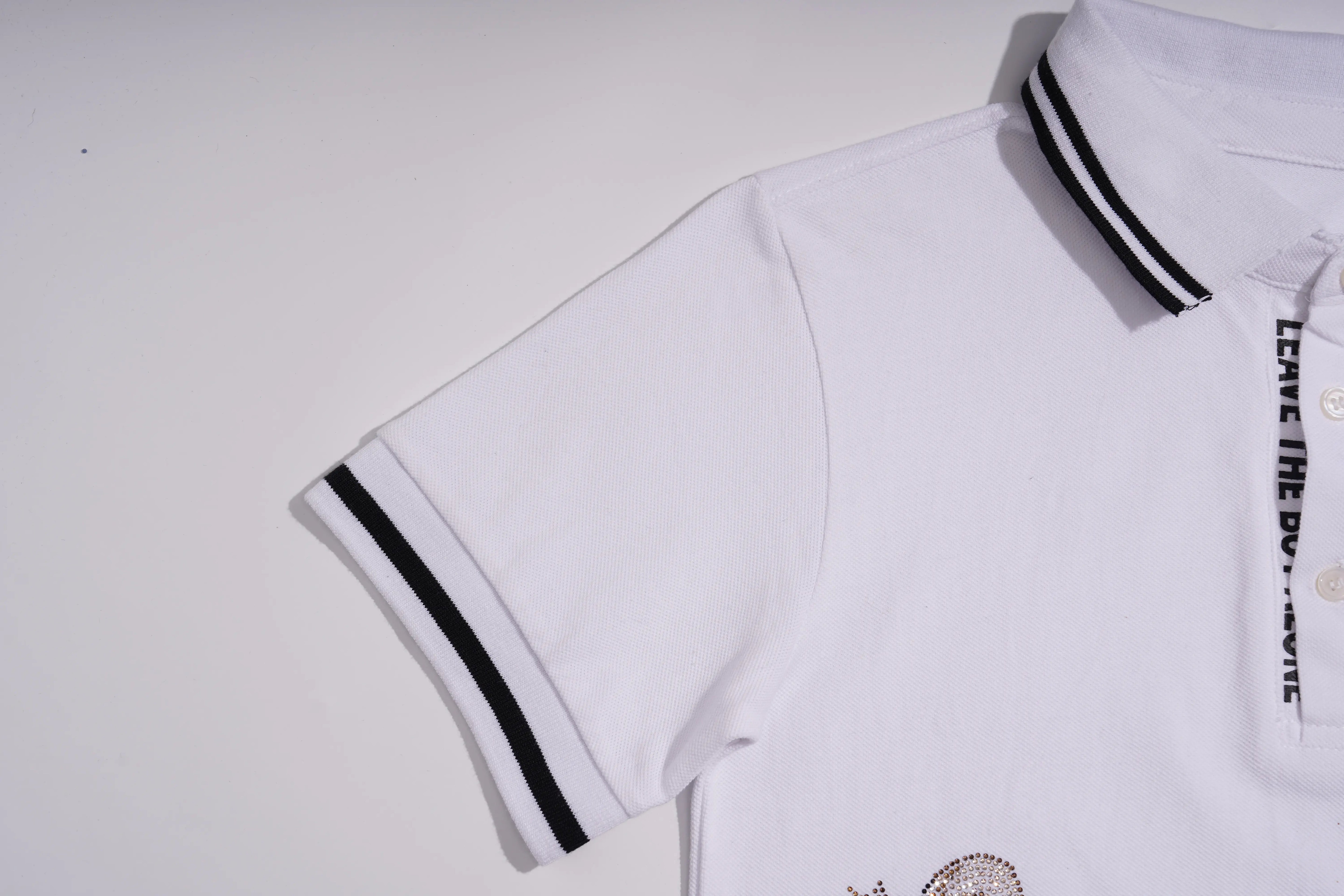 White short-sleeve polo shirt with black double-striped collar and sleeve cuffs, featuring vertical black text on the chest and a small circular graphic near the lower hem. TCH White Teddy Bear Embellished Polo Shirt