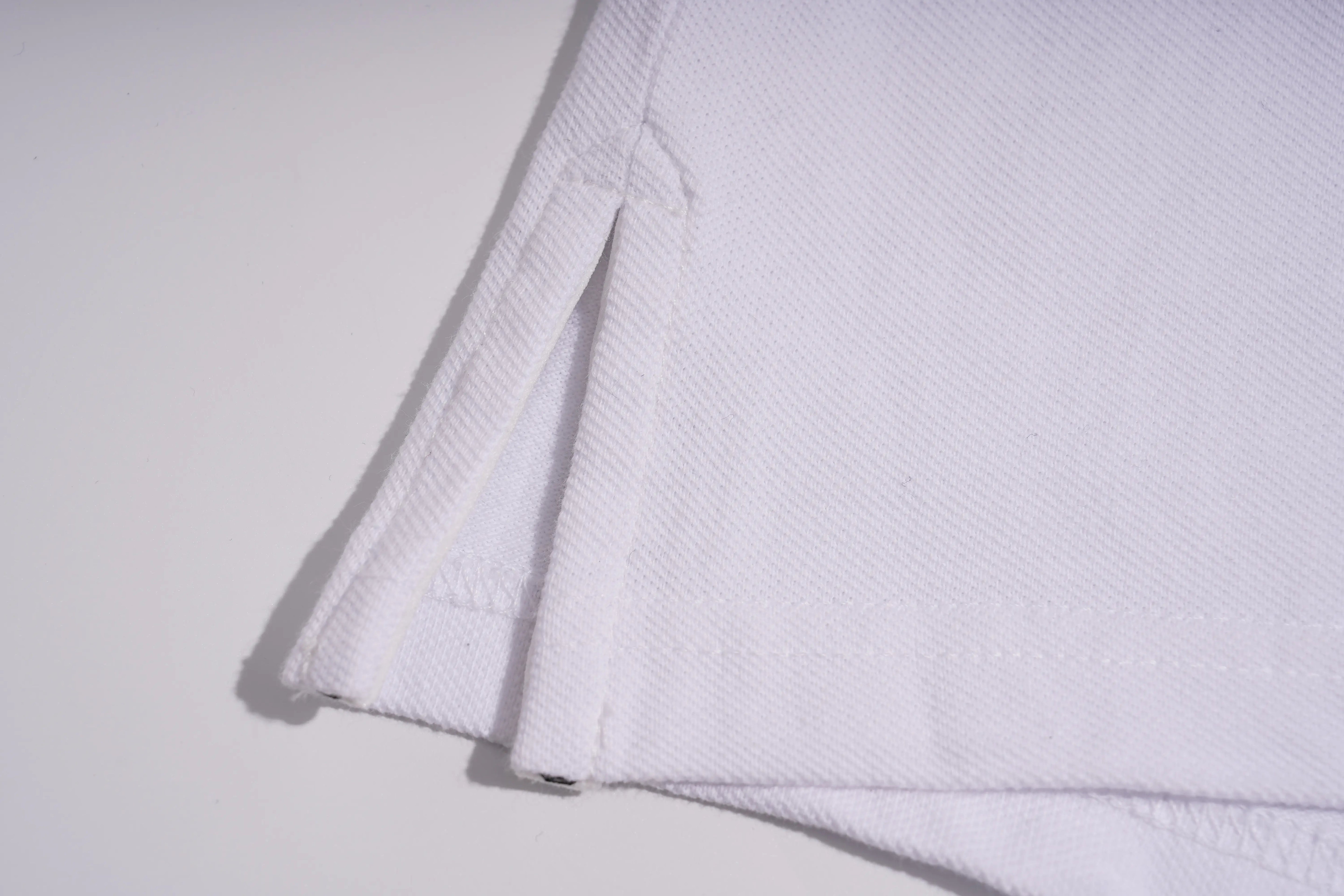 Close-up of a folded white woven fabric, showing the texture and a stitched edge on a light gray background. TCH White Teddy Bear Embellished Polo Shirt