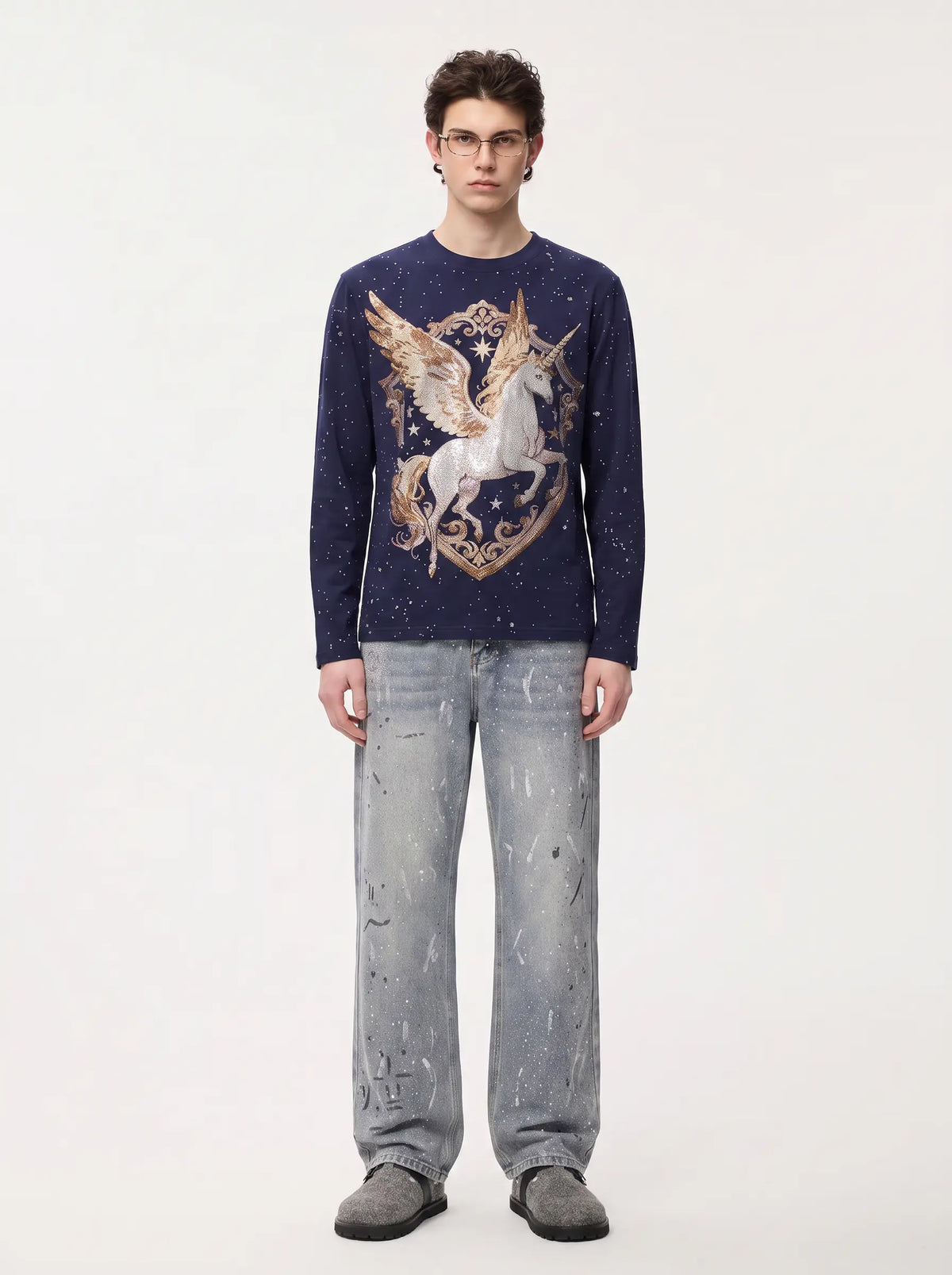 A man wearing a navy blue long-sleeve crewneck sweater with a large gold and white pegasus graphic on the front, paired with light-wash distressed jeans and dark gray slip-on shoes, standing against a plain white studio background. TCH Winged Unicorn Starry Rhinestone Long Sleeve T-Shirt