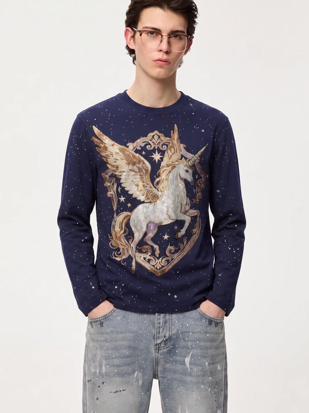 A man wearing a navy blue long-sleeve crewneck sweater with a large graphic of a white pegasus unicorn inside an ornate gold crest, paired with light-wash jeans, against a plain light gray background. TCH Winged Unicorn Starry Rhinestone Long Sleeve T-Shirt