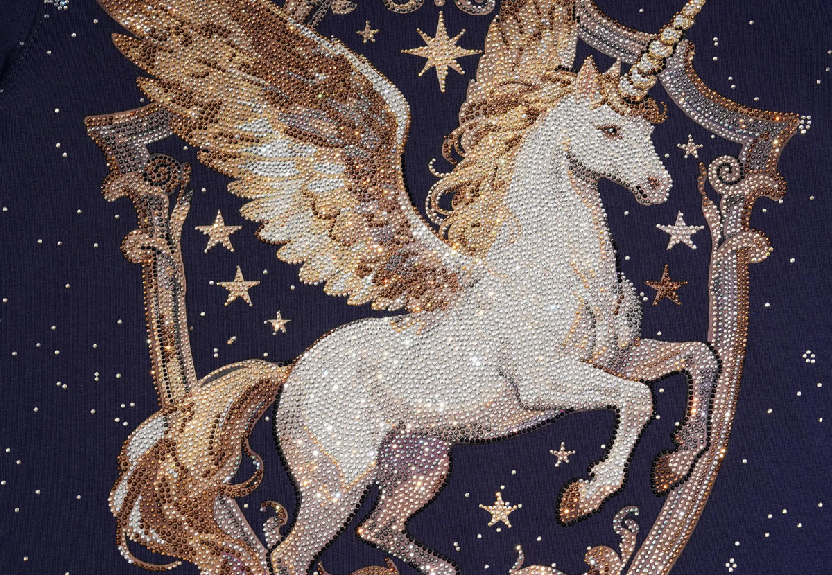 Close-up of a rhinestone-embellished unicorn design on a dark navy fabric background, featuring a white unicorn with gold wings and stars. TCH Winged Unicorn Starry Rhinestone Long Sleeve T-Shirt