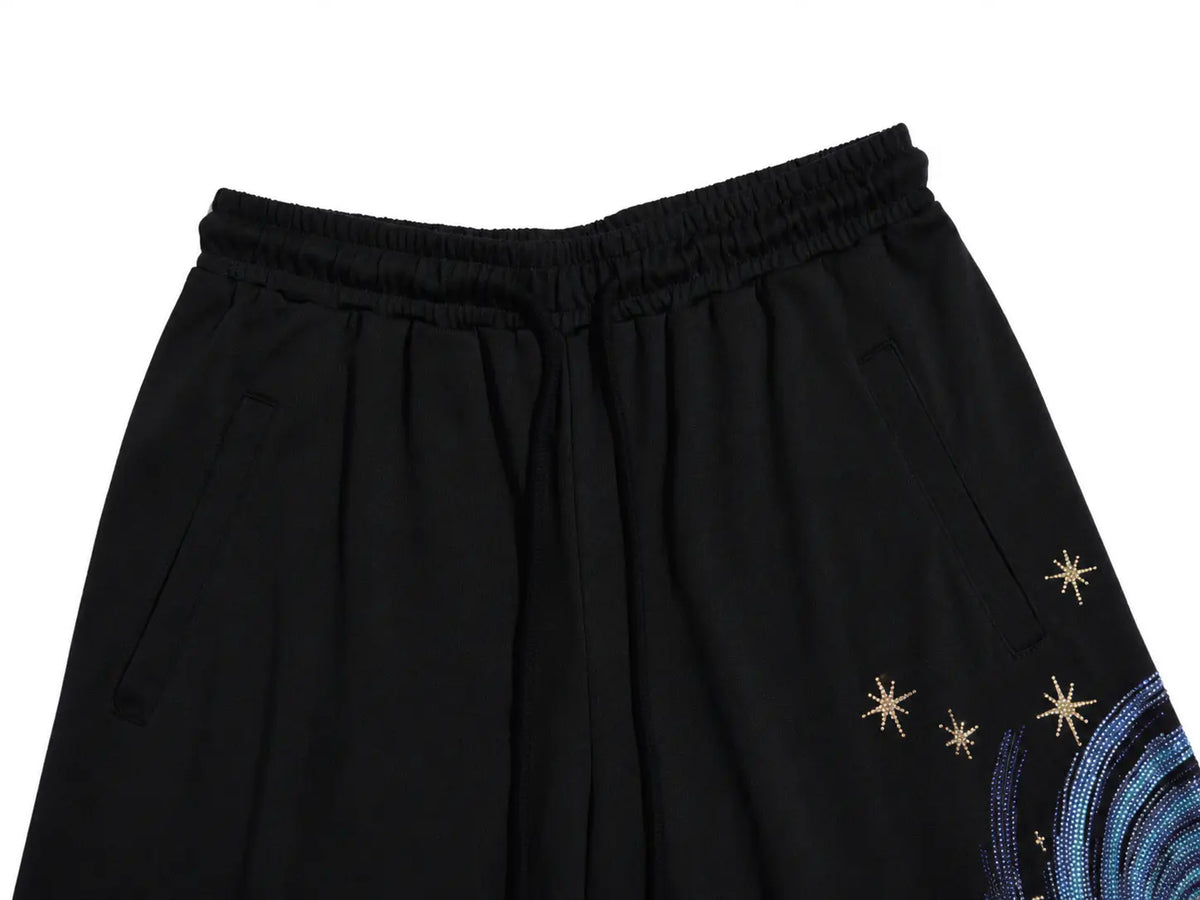 Black wide-leg pants featuring an elastic waistband, side pockets, and embroidered celestial details including gold stars and a blue moon pattern on the lower right leg. TCH Women’s Black Wide-Leg Sweatpants with Rhinestone Star Graphic