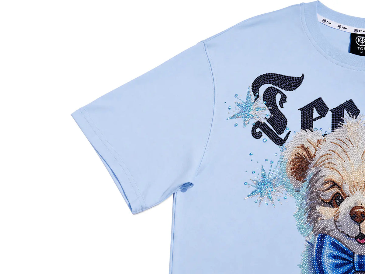A light blue short-sleeve t-shirt featuring a large graphic print of a teddy bear wearing a blue bow tie, accented with sparkling black and blue lettering and star details, shown against a plain white background. TCH Women's Blue Teddy Bear Graphic Oversized T-Shirt