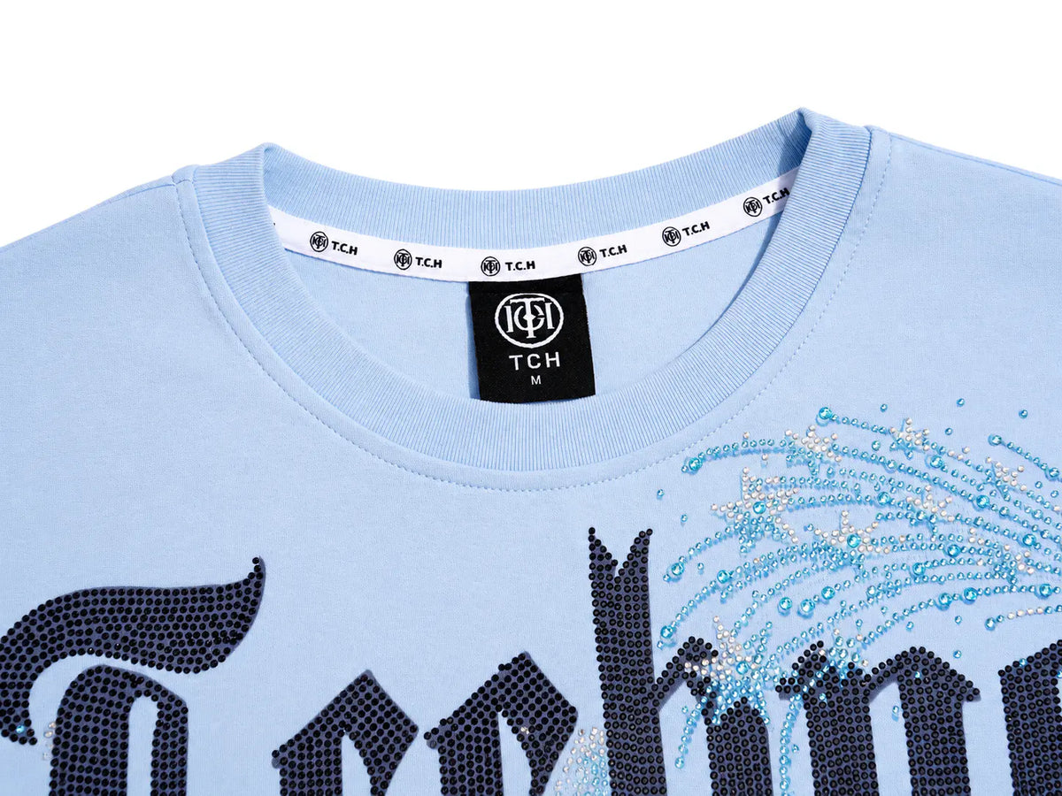 Close-up of a light blue T-shirt with a black neck label reading TCH, and a rhinestone graphic on the front in dark and light blue tones. TCH Women's Blue Teddy Bear Graphic Oversized T-Shirt