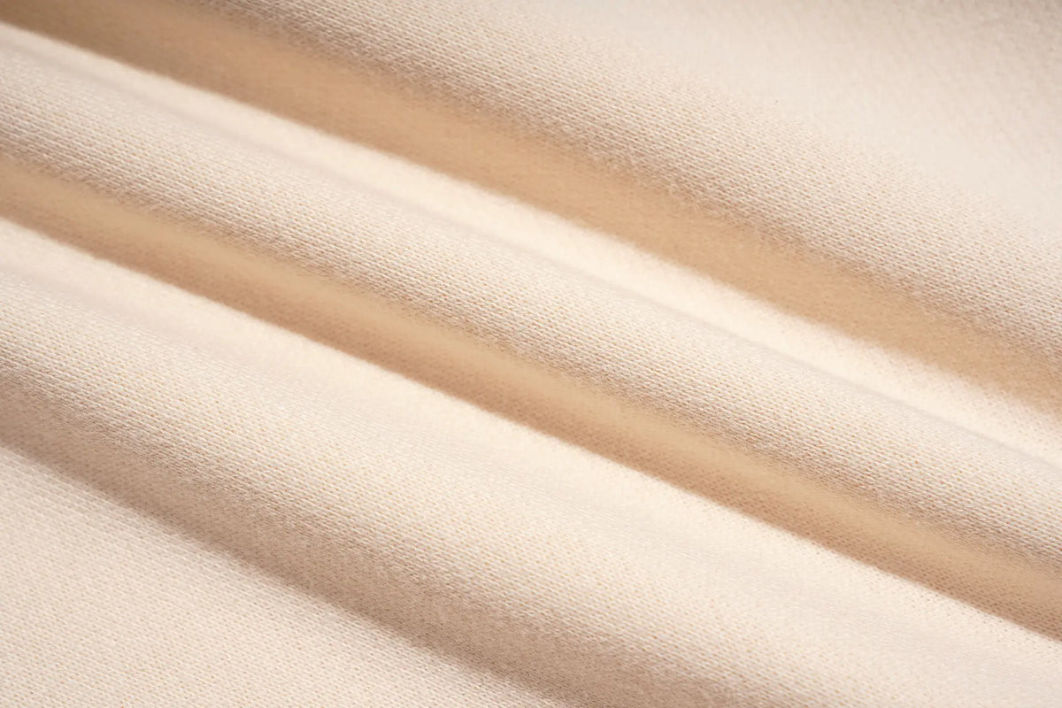 A close-up of draped cream-colored fabric with soft folds and a fine woven texture. TCH Women’s Cream Cargo Sweatpants with Teddy Bear Rhinestone Graphic