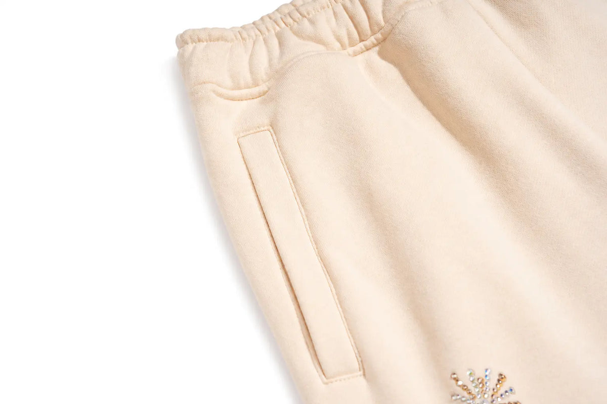 Close-up of a cream-colored fleece sweatshirt showing the elastic waistband, a side pocket, and a small embroidered logo on the lower corner. TCH Women’s Cream Cargo Sweatpants with Teddy Bear Rhinestone Graphic