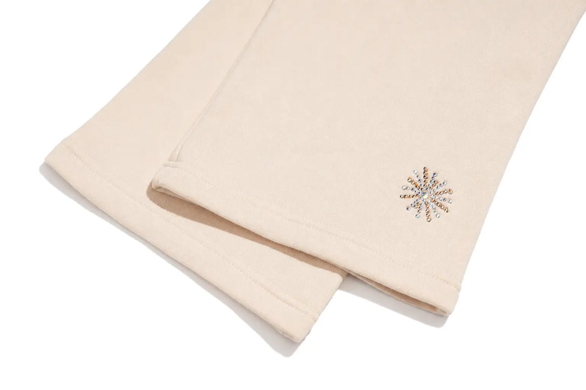 A close-up of a light beige fabric item, likely a sweatshirt or jacket sleeve, featuring a small embroidered multicolor snowflake design on the cuff. TCH Women’s Cream Cargo Sweatpants with Teddy Bear Rhinestone Graphic