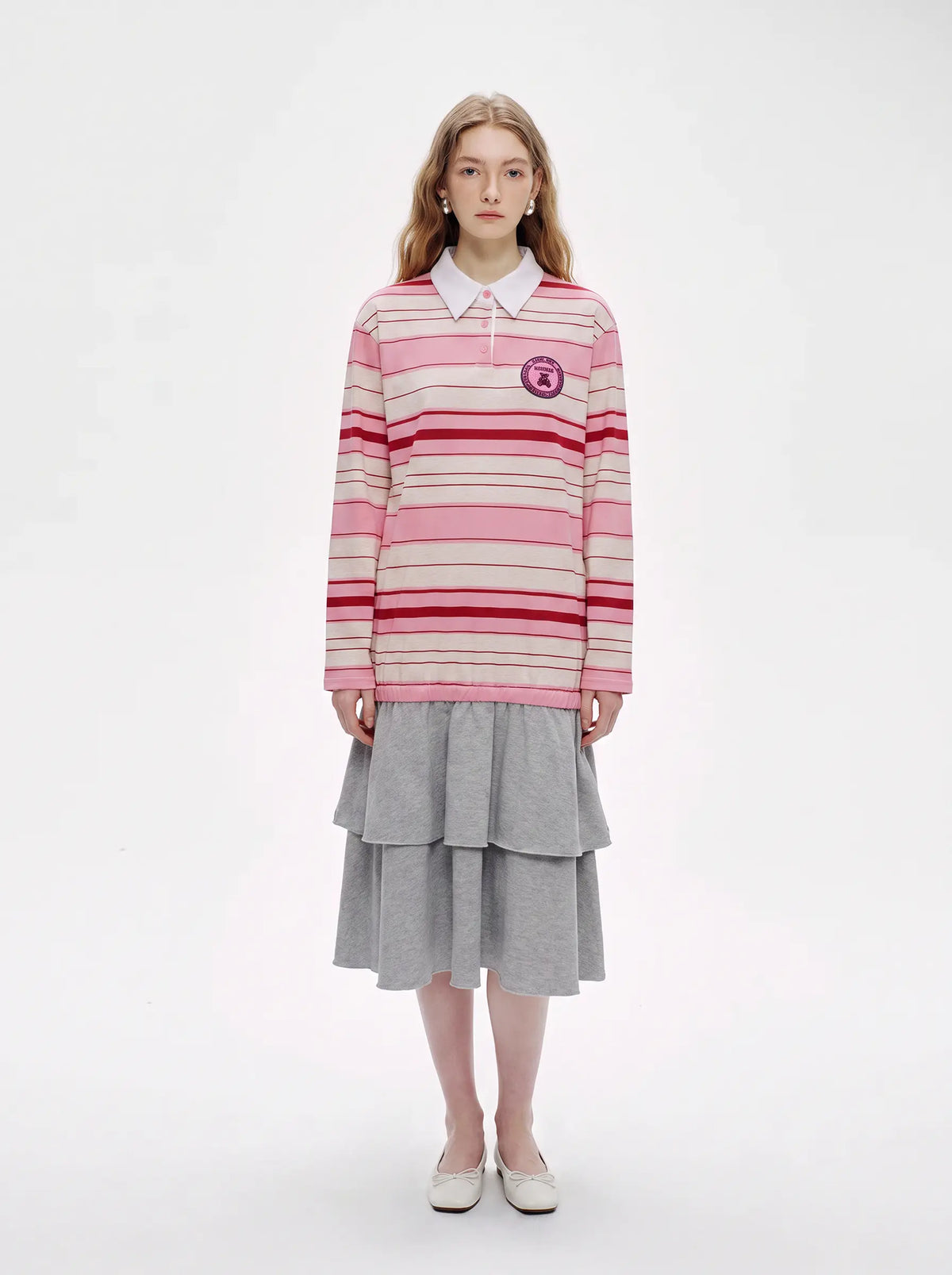 A model stands against a plain white studio background wearing a pink and red striped long-sleeve polo shirt with a white collar, paired with a gray tiered skirt and white shoes. TCH Women's Striped Polo Mini Dress